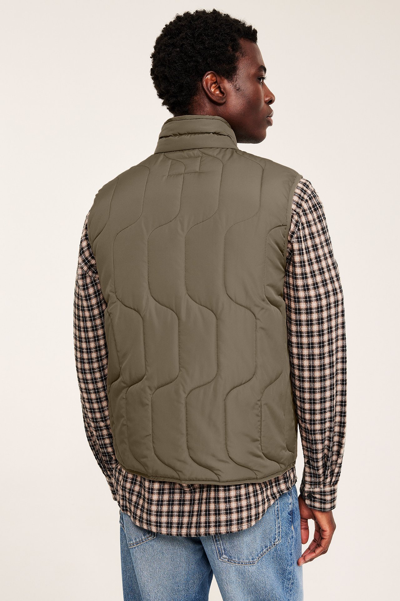 Ryggvy av en man i en brun quiltad väst, över en rutig skjorta och blå jeans.