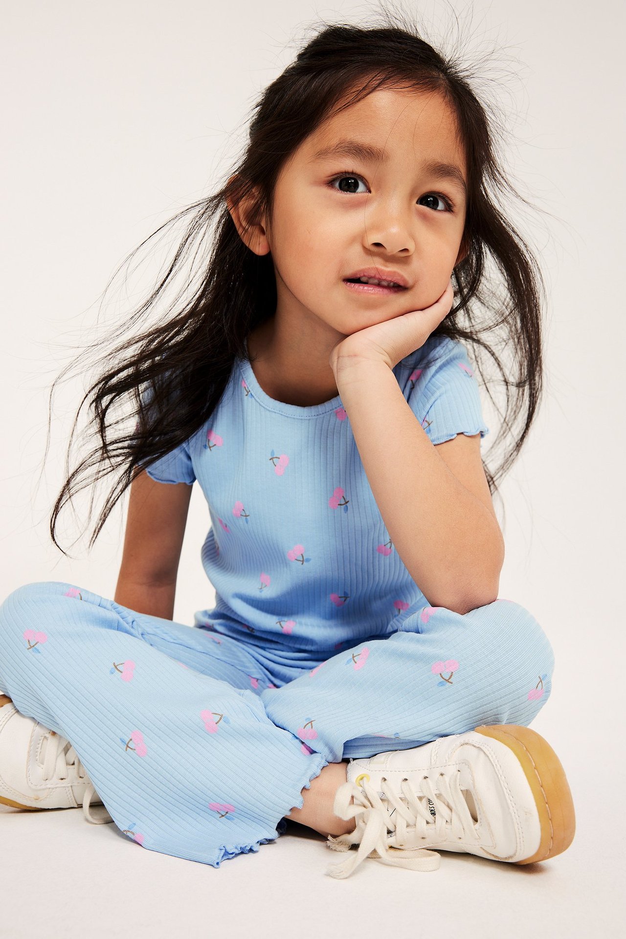 Edestäpäin: Lapsi vaaleansinisessä ribbitoppissa ja yhteensopivissa kirsikkaprinttihousuissa, valkoiset tennarit jalassa.