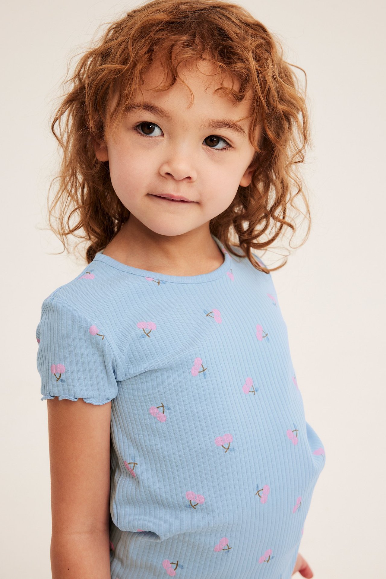 Widok z przodu: dziecko w jasnoniebieskim prążkowanym topie z różowymi wiśniami i rękawami babylock.