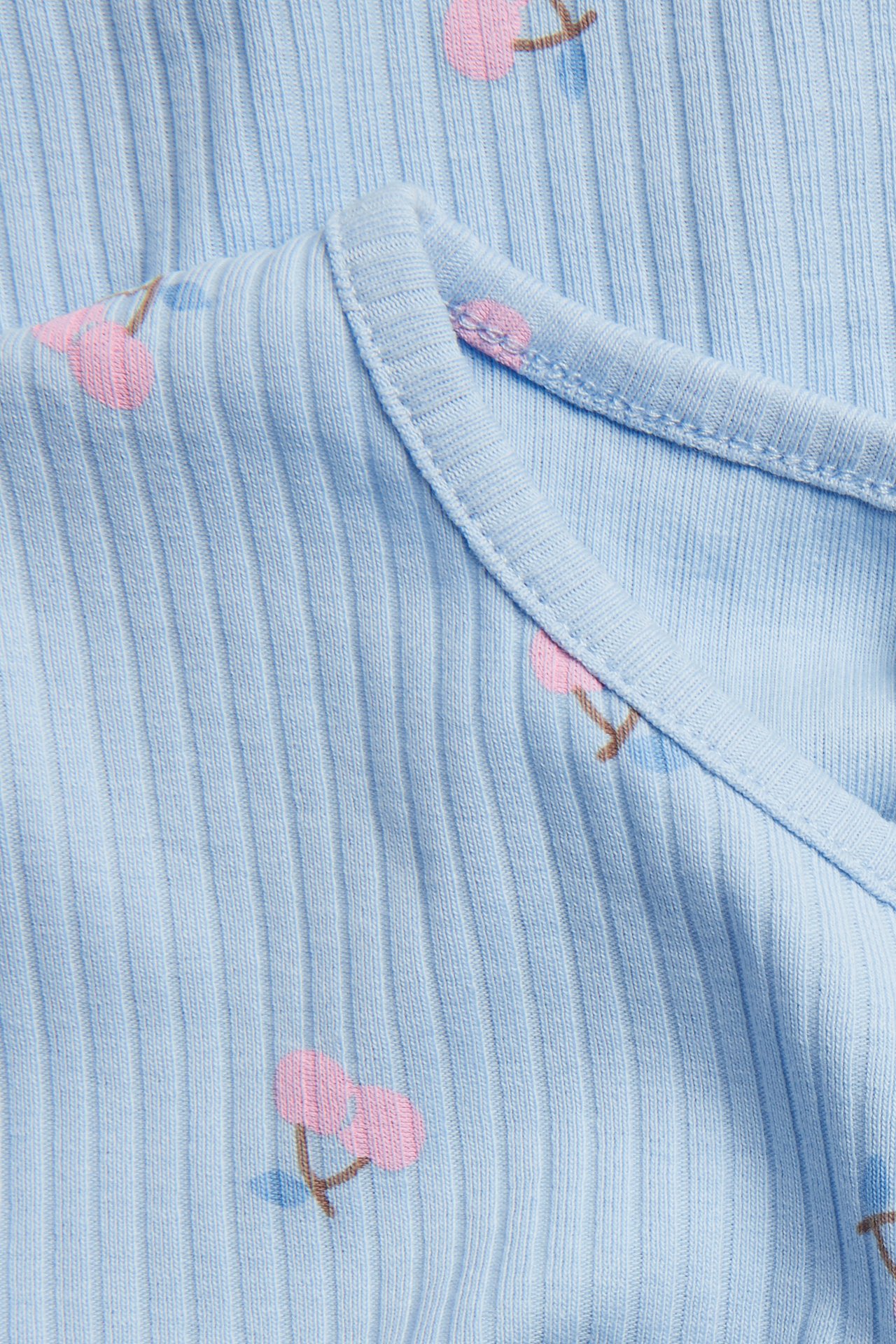 Lähikuva vaaleansinisestä ribbipaidasta, jossa on kauttaaltaan vaaleanpunainen kirsikkakuvio.