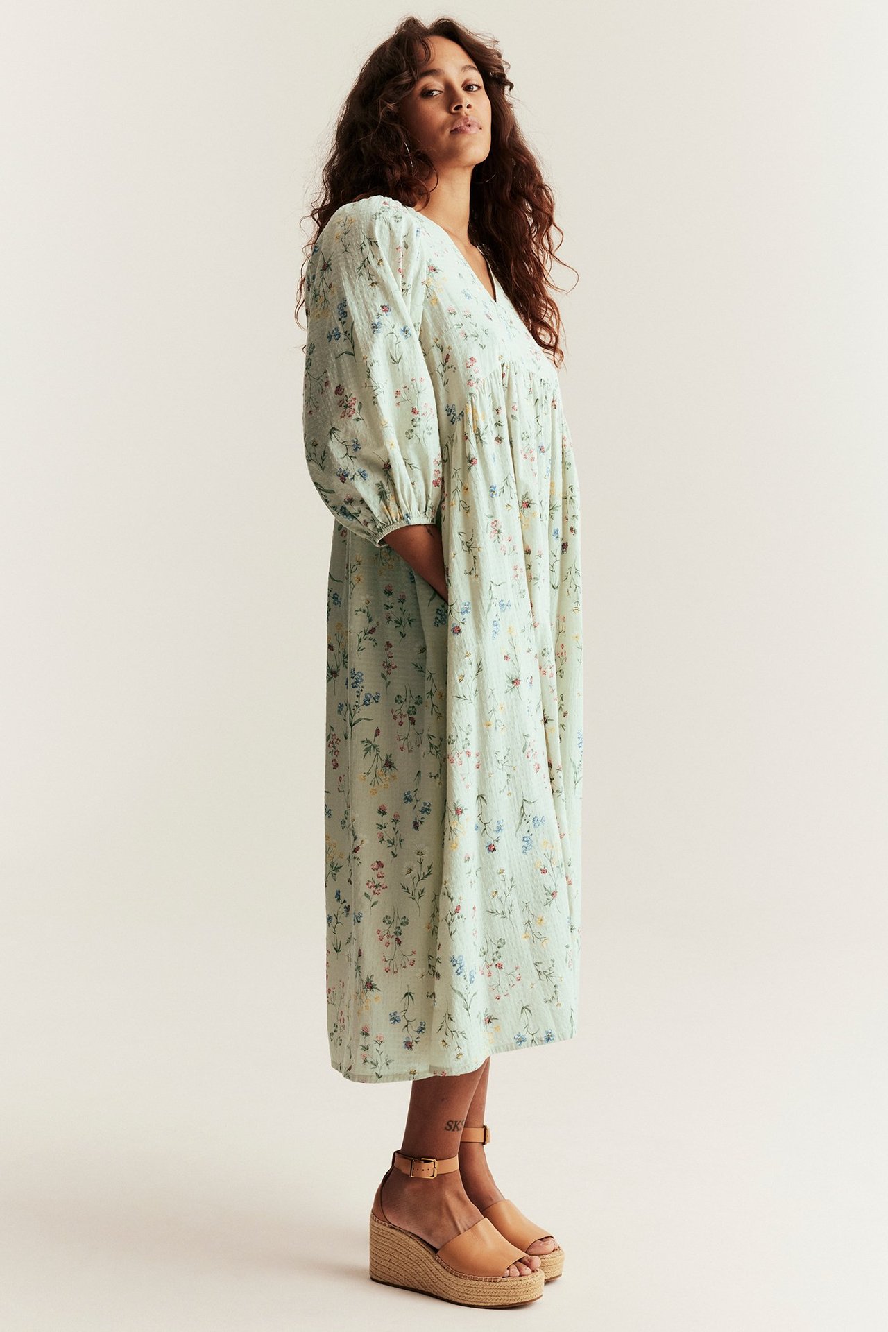 Sivukuva: Nainen yllään vaaleanvihreä kukkakuvioinen puuvillamekko puffihihoilla ja espadrillikiilasandaaleilla.