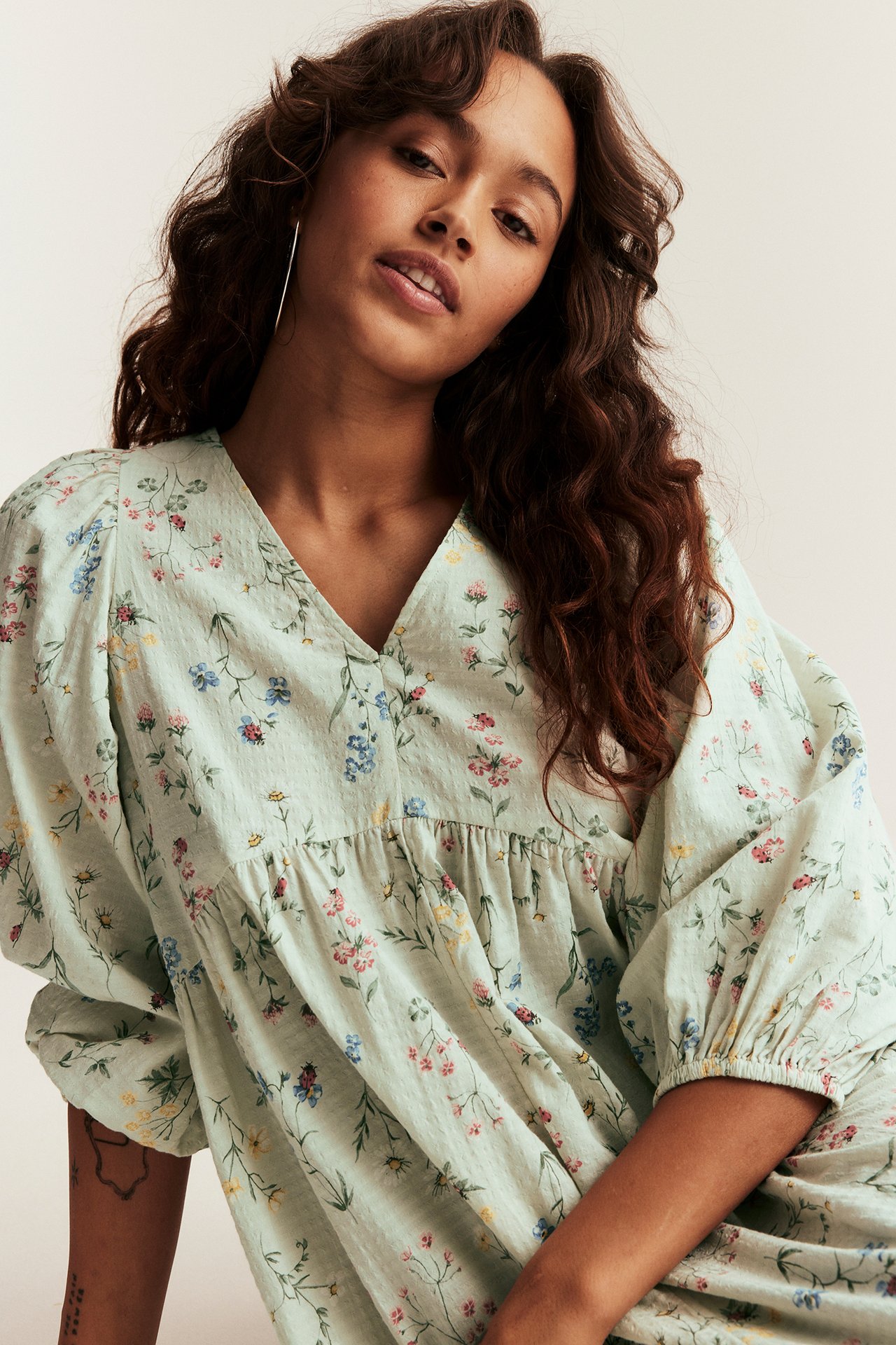 Lähikuva naisesta vaaleanvihreässä kukkakuvioisessa puuvillamekossa, v-pääntie ja pussihihat.