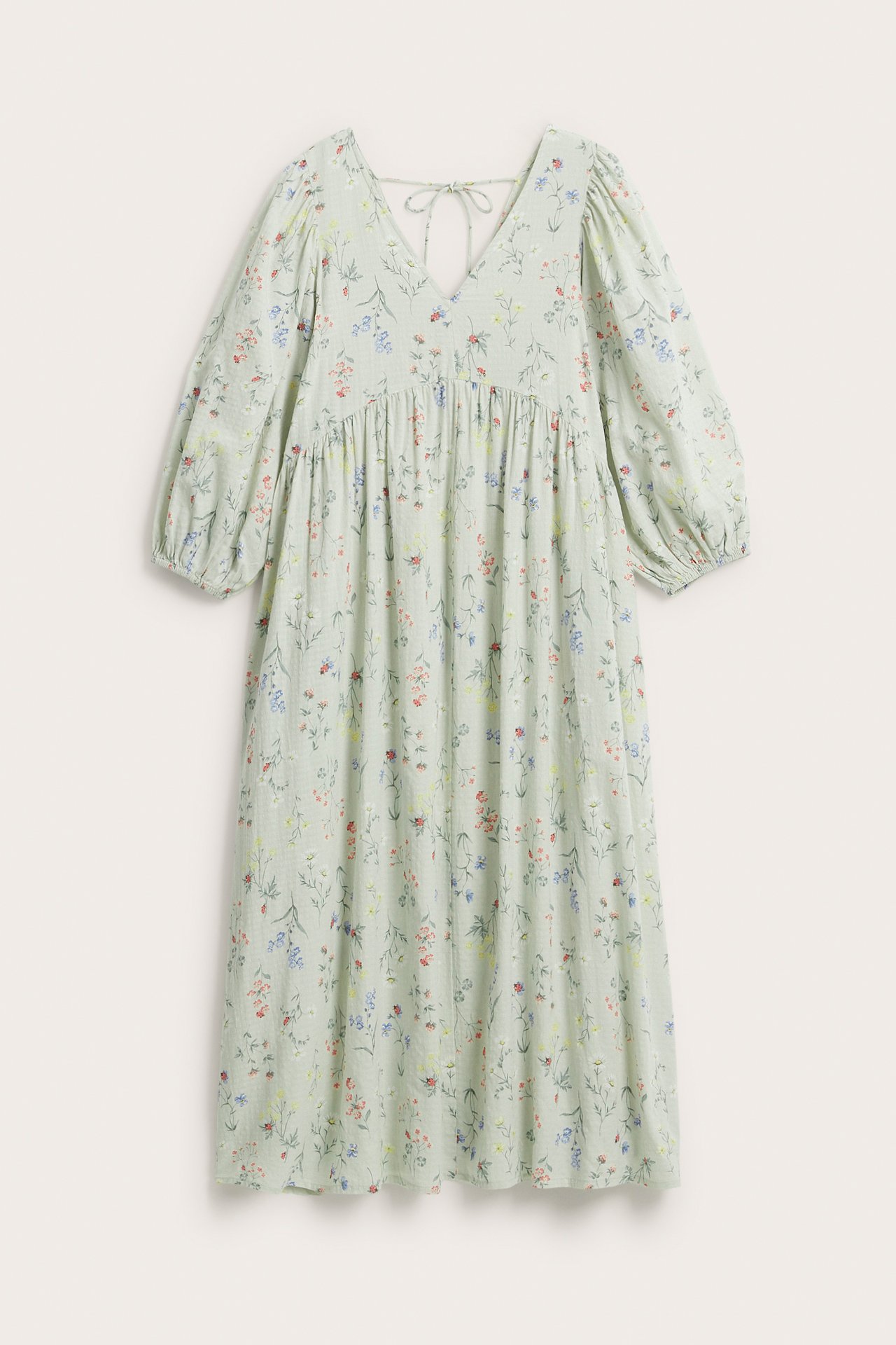Frontvisning av lys grønn blomstret bomullskjole med V-hals, 3/4 puffermer og knytebånd bak.