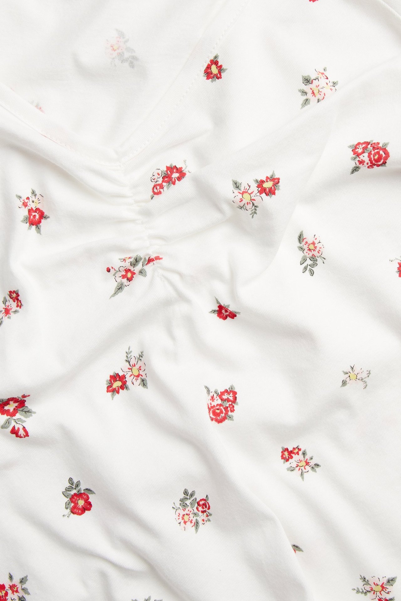 Zbliżenie na ecru bawełnianą koszulę nocną z drobnym czerwonym wzorem kwiatowym i marszczeniem z przodu.