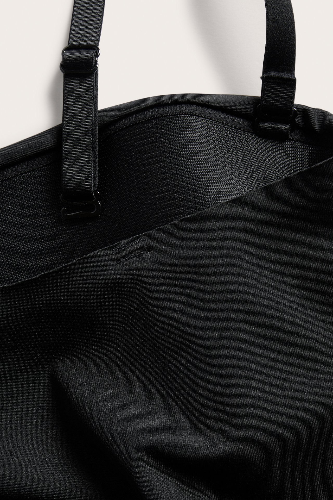 Närbild av en svart vadderad stringbody med justerbara band och mjuk microkvalitet.