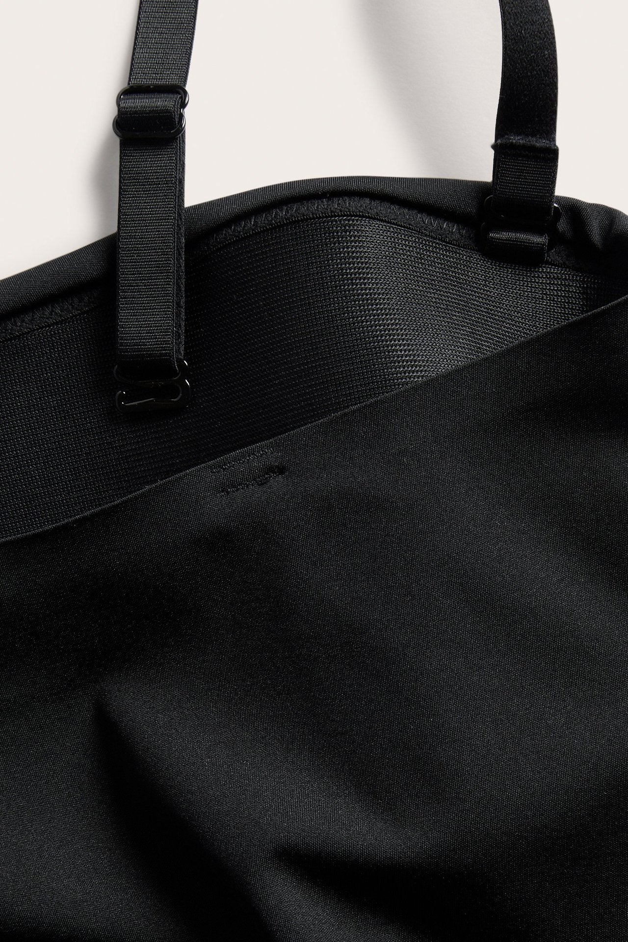 Närbild av en svart vadderad stringbody med justerbara band och mjuk microkvalitet.