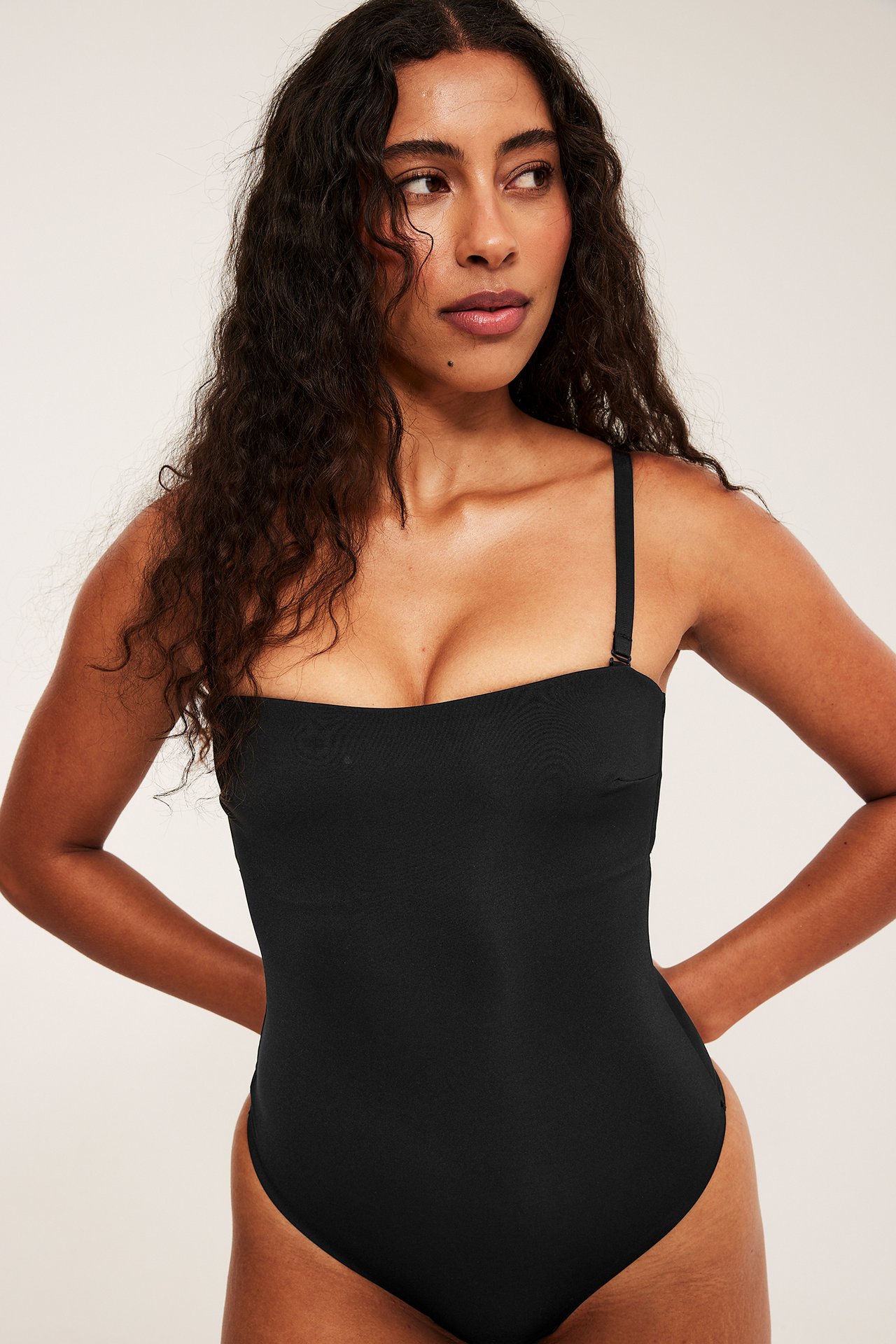 Frontbilde av kvinne i svart polstret stringbody med avtakbare stropper, laget av glatt, elastisk stoff.