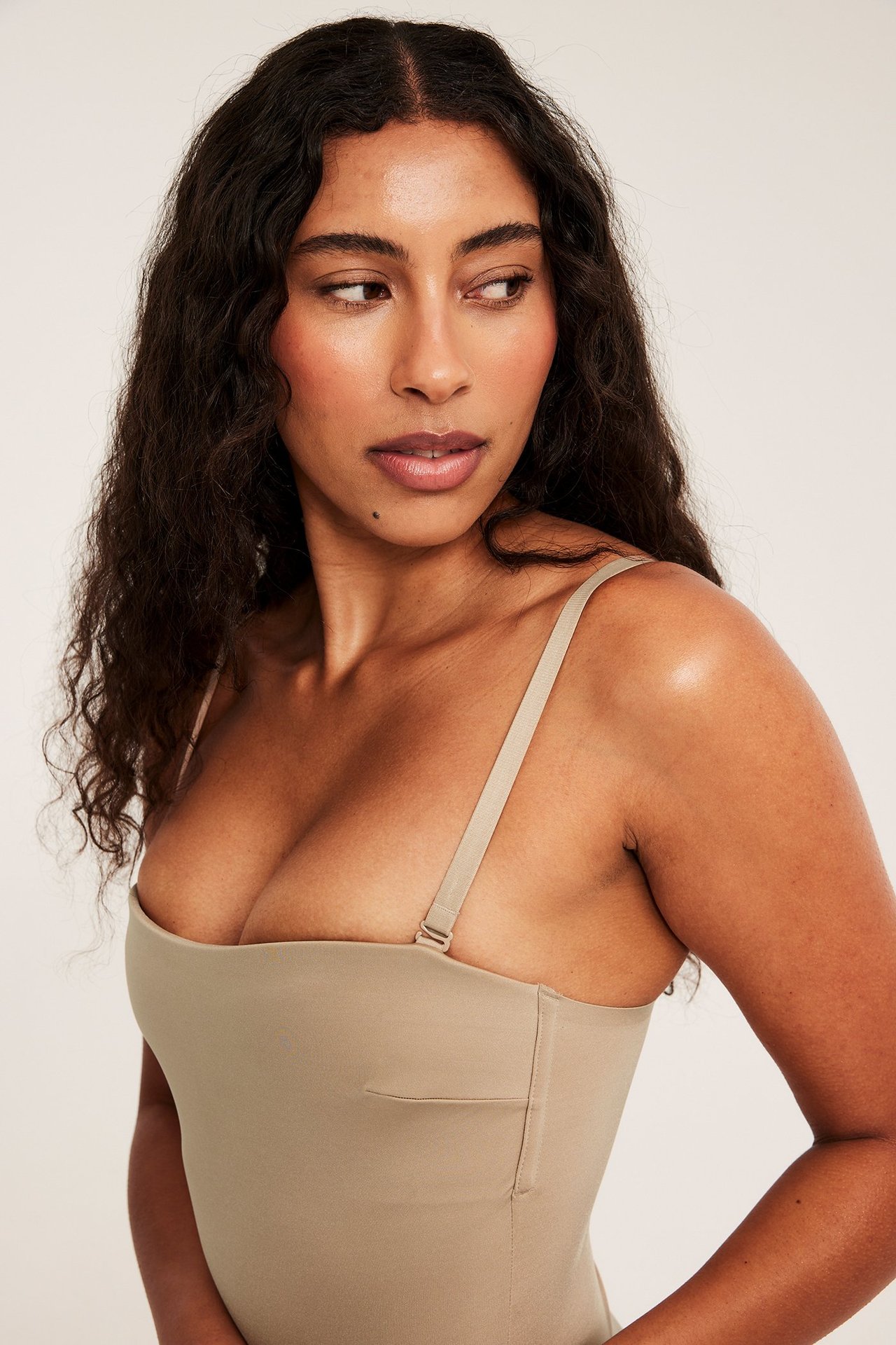 Nærbilde av en kvinne iført en lys brun stringbody med vatterte skåler og justerbare stropper.