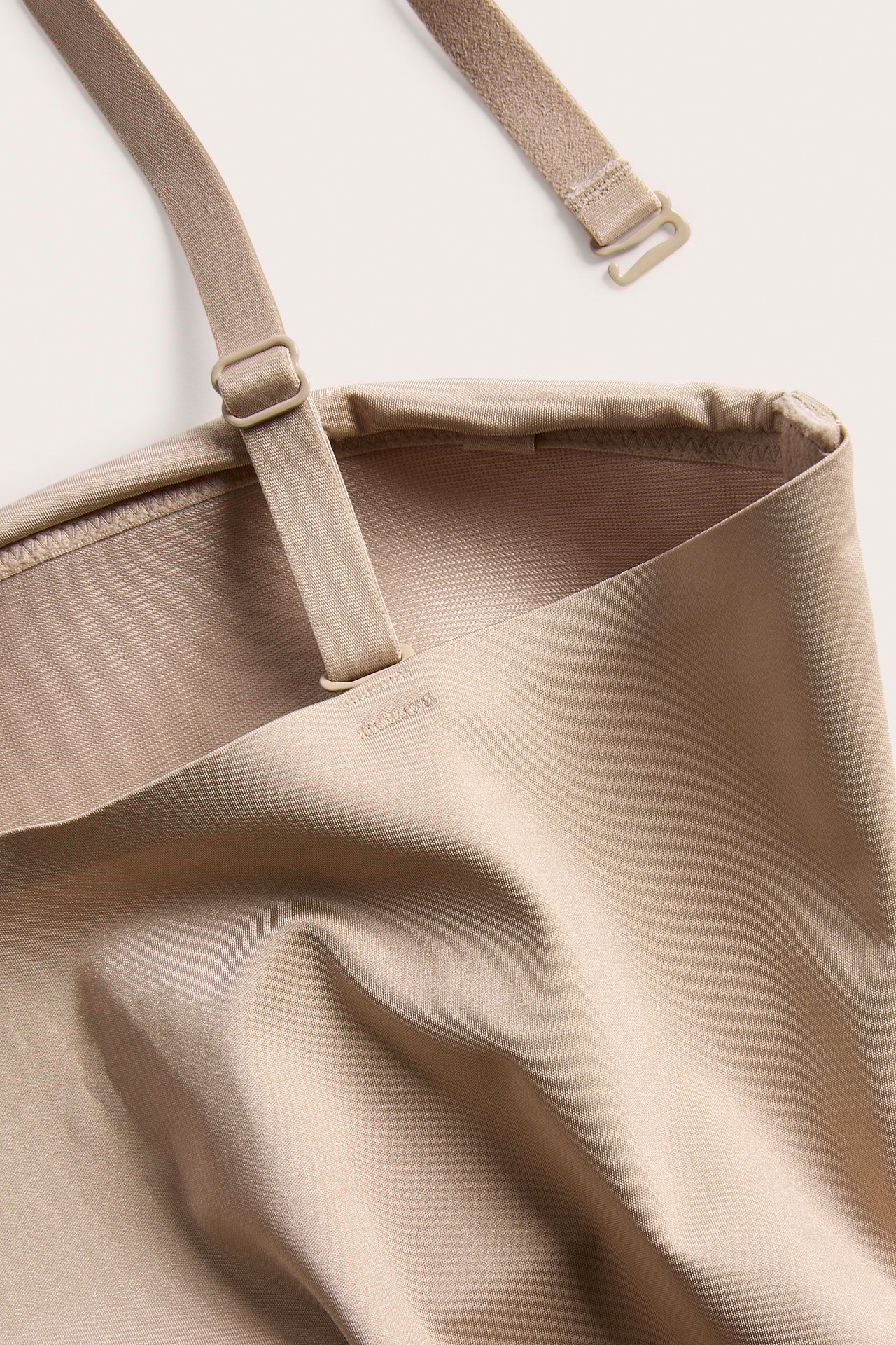 Närbild, uppifrån, av en beige enfärgad shapewear-body med en justerbar, avtagbar axelrem.