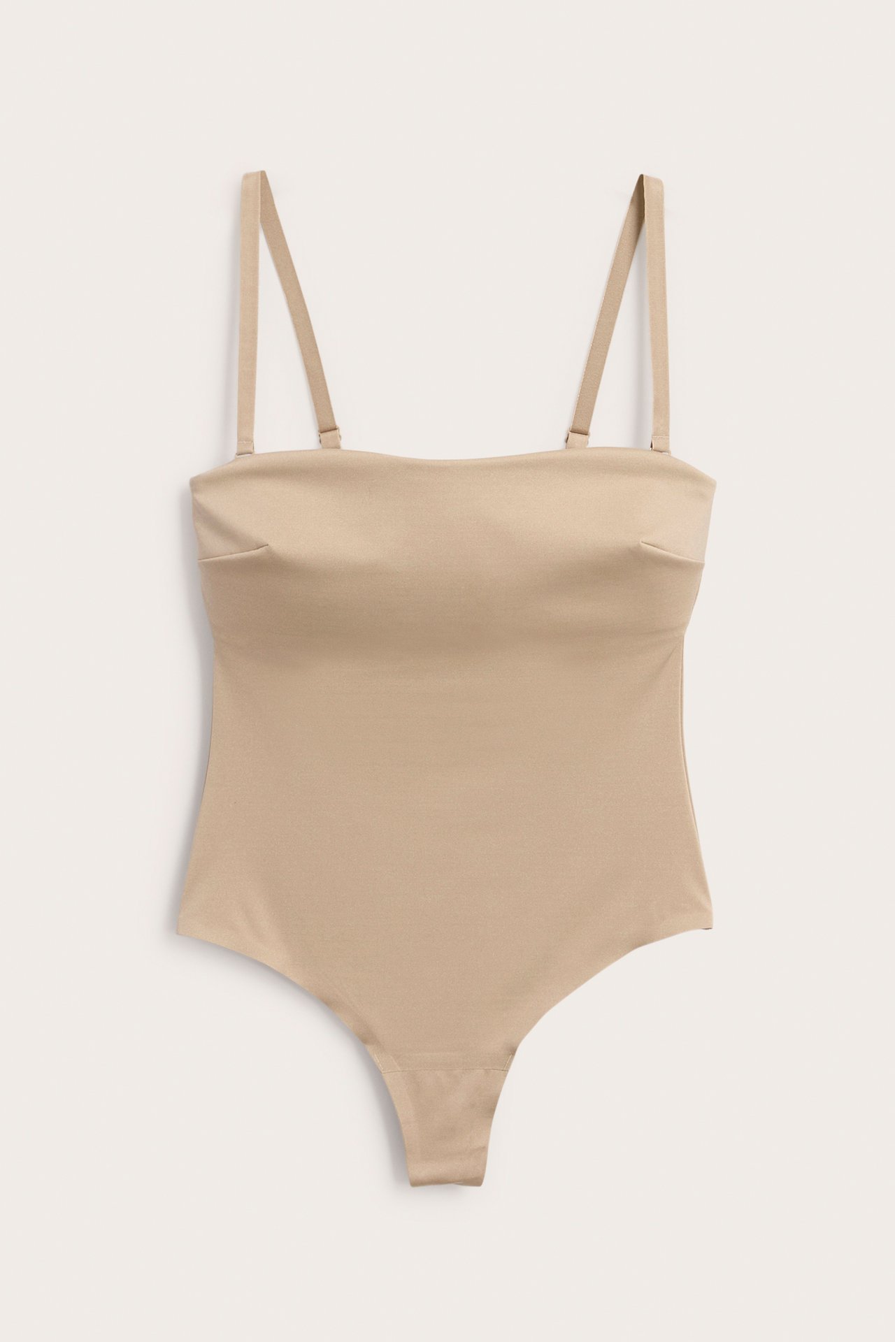 Frontvy: Ljusbeige vadderad stringbody i stretchig micro med avtagbara, justerbara band.