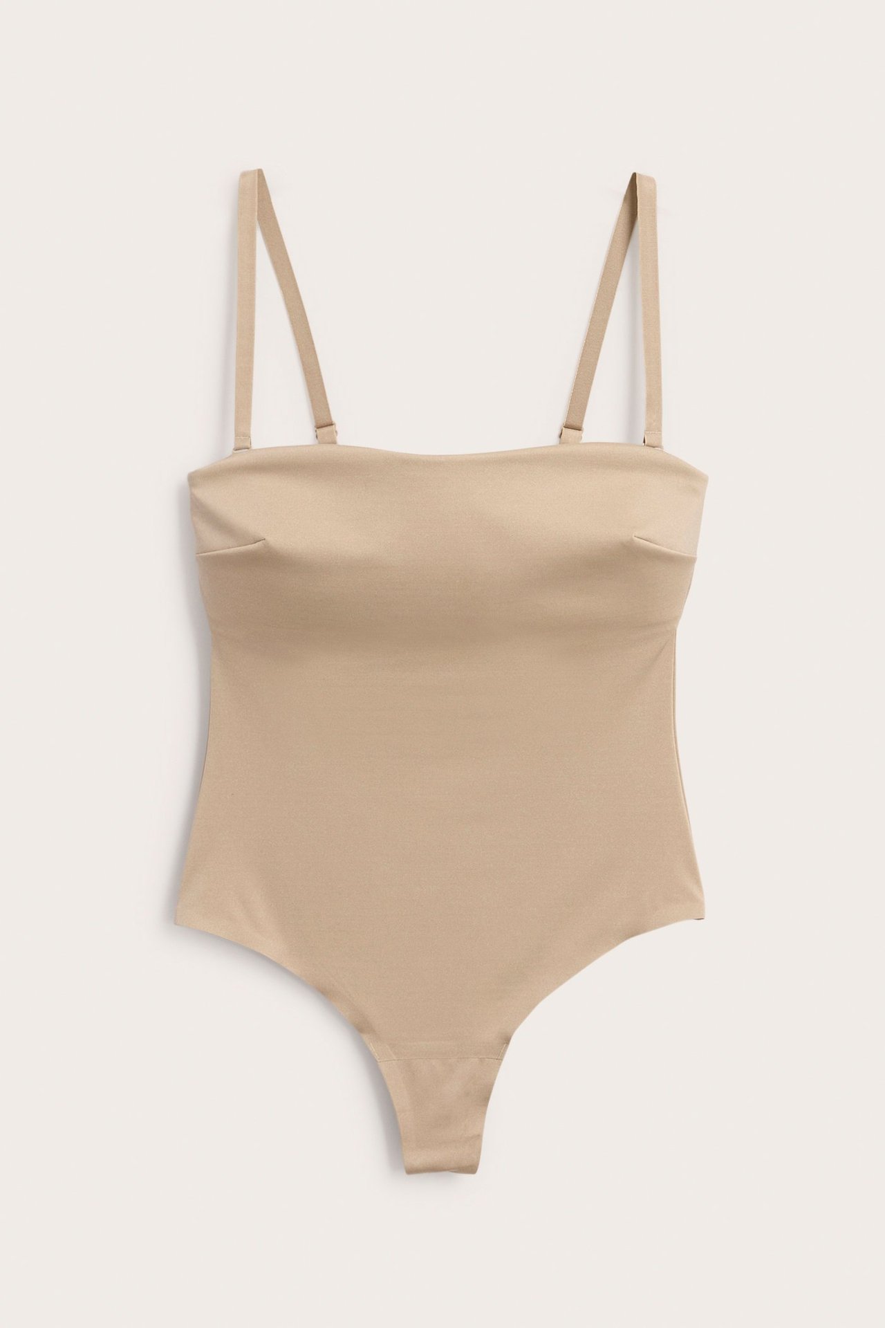 Frontvy: Ljusbeige vadderad stringbody i stretchig micro med avtagbara, justerbara band.