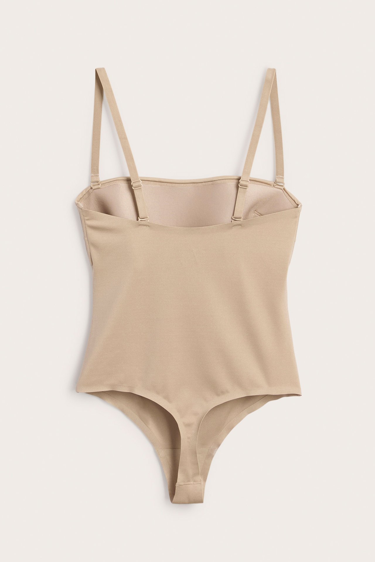 Frontvy av en beige vadderad stringbody i mjuk stretchig mikrofiber med avtagbara axelband.