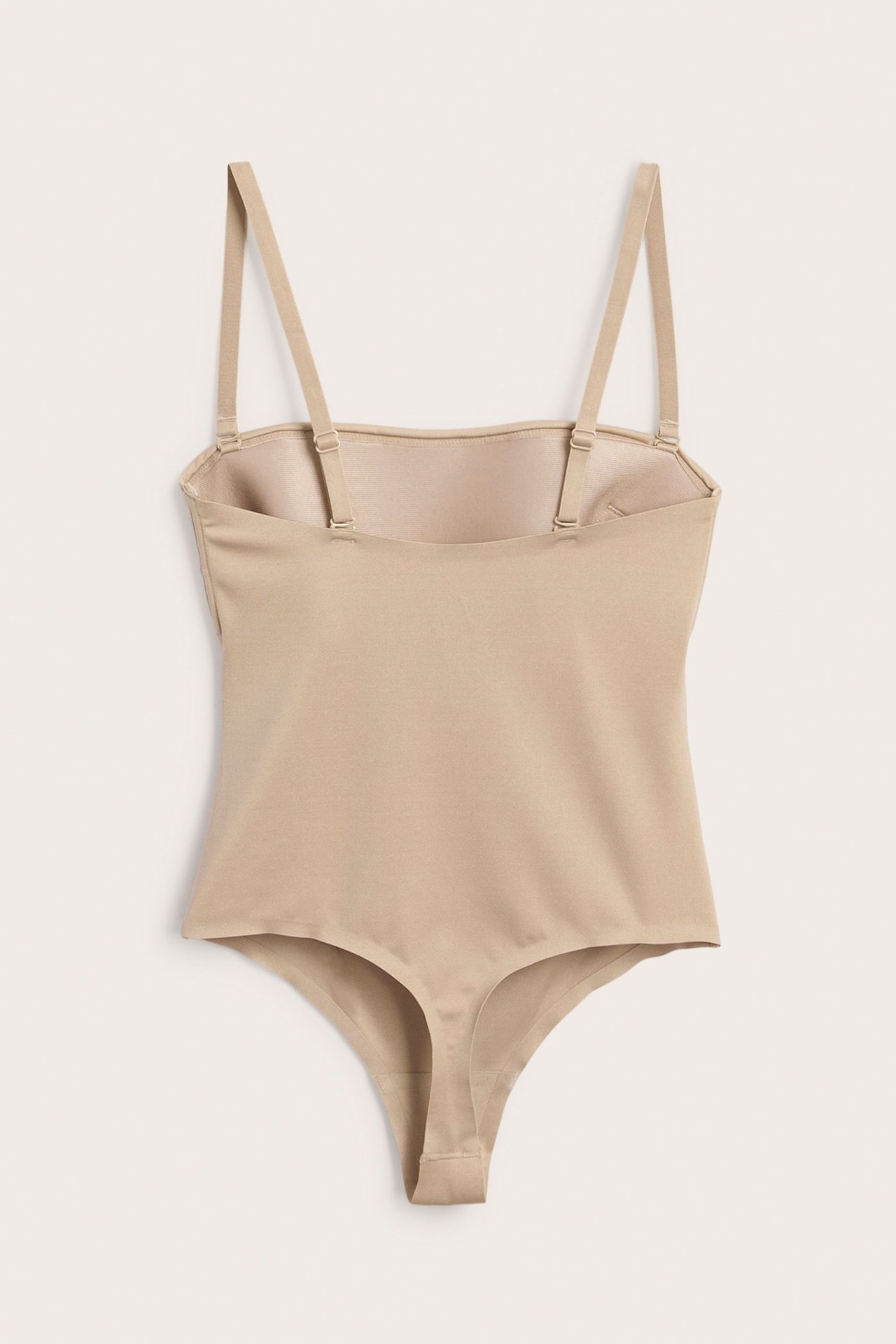 Frontvy av en beige vadderad stringbody i mjuk stretchig mikrofiber med avtagbara axelband.