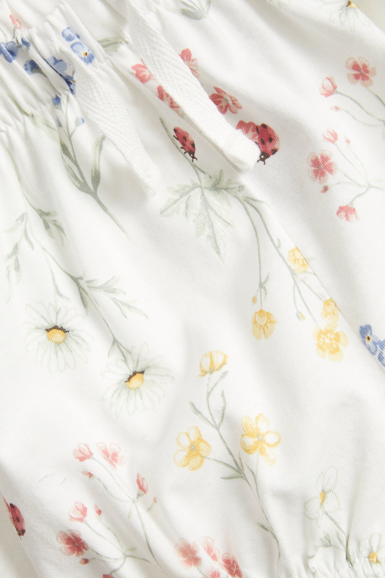 Närbild på offwhite blommiga jerseyshorts med nyckelpigor, resår, dragsko i midjan och volang i benslut.