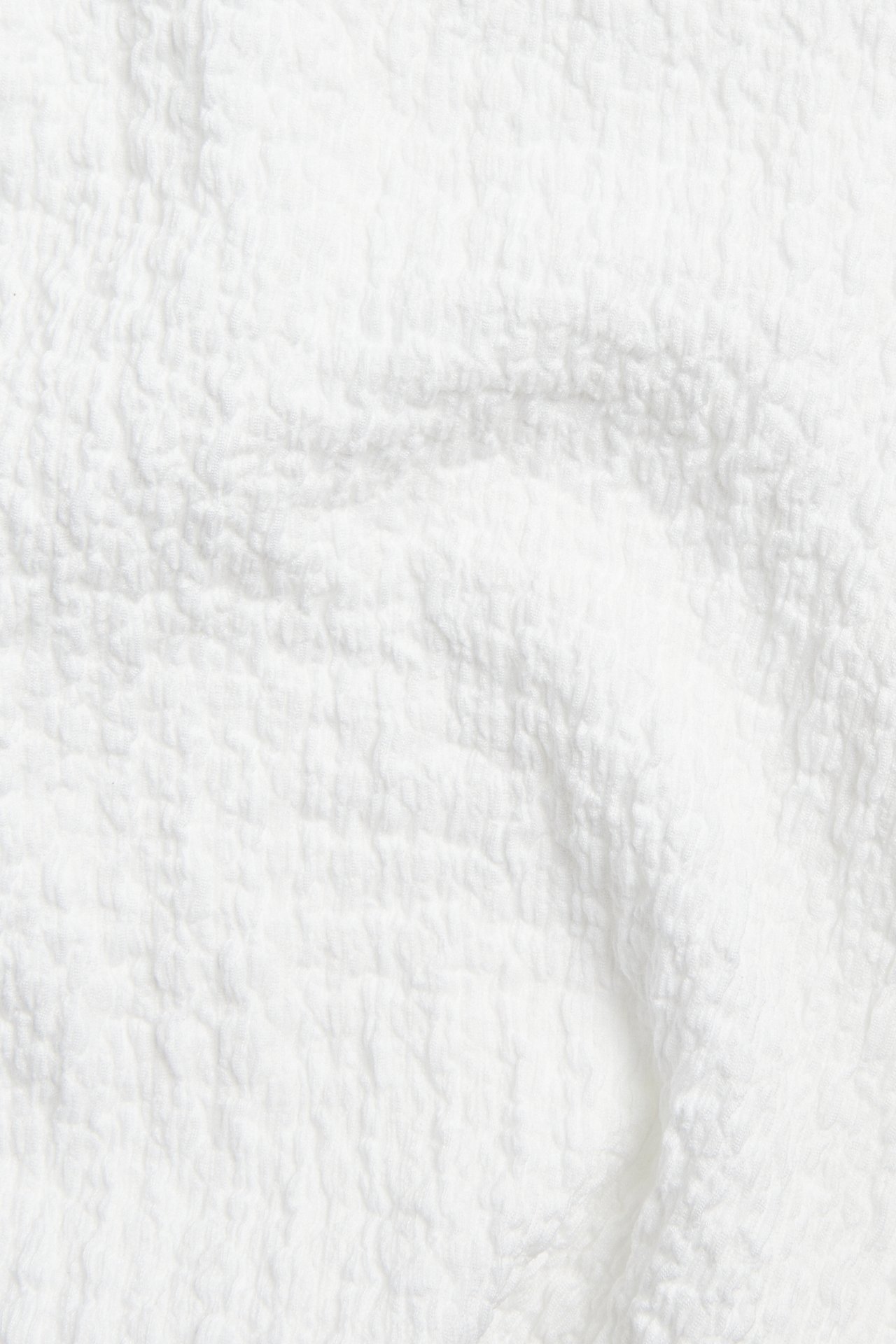 Zbliżenie białej, teksturowanej tkaniny, prawdopodobnie poliestru, z efektem marszczenia lub bukle.