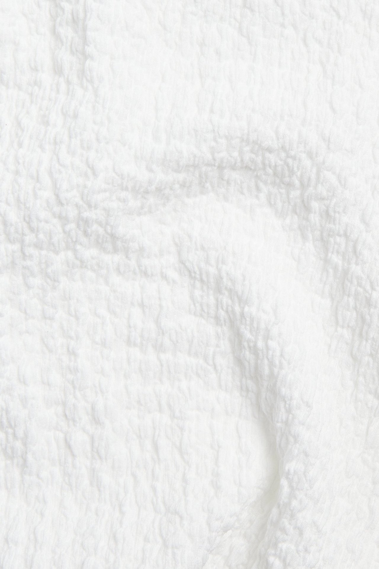 Zbliżenie białej, teksturowanej tkaniny, prawdopodobnie poliestru, z efektem marszczenia lub bukle.