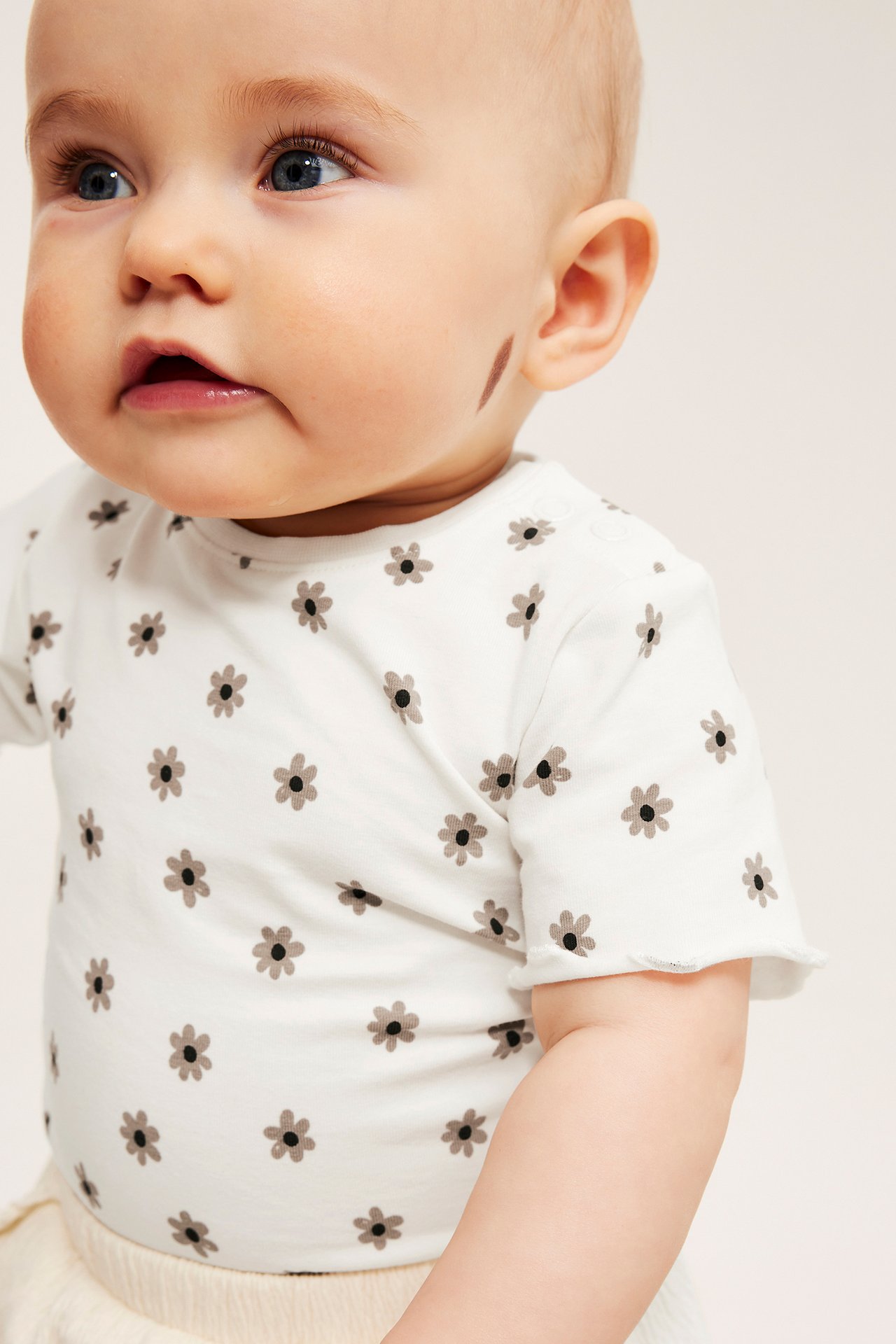 Lähikuva sivulta vauvasta yllään luonnonvalkoinen lyhythihainen body pienellä kukkakuviolla.