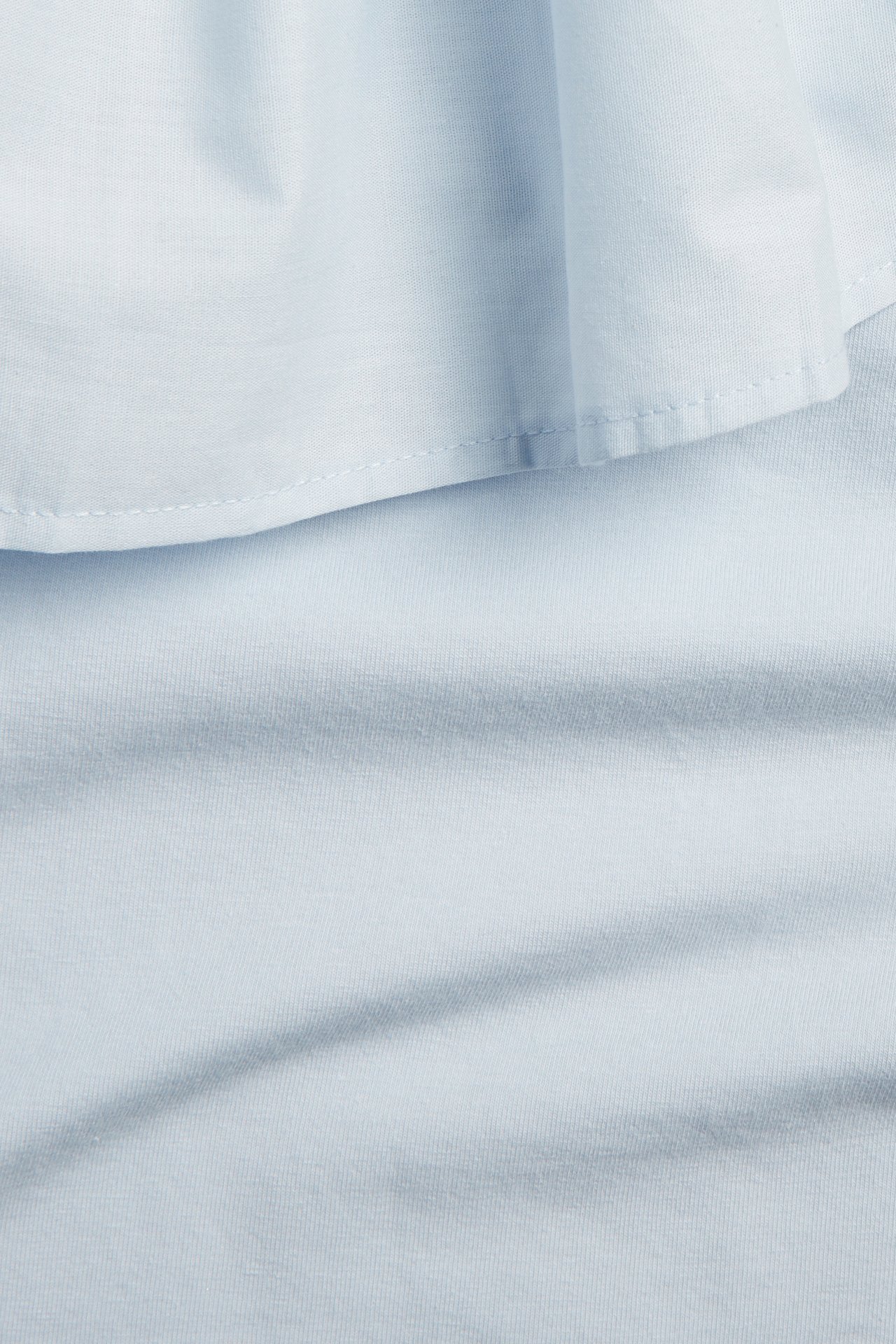 Zbliżenie na jasnoniebieski bawełniany top z falbanką na jedno ramię.