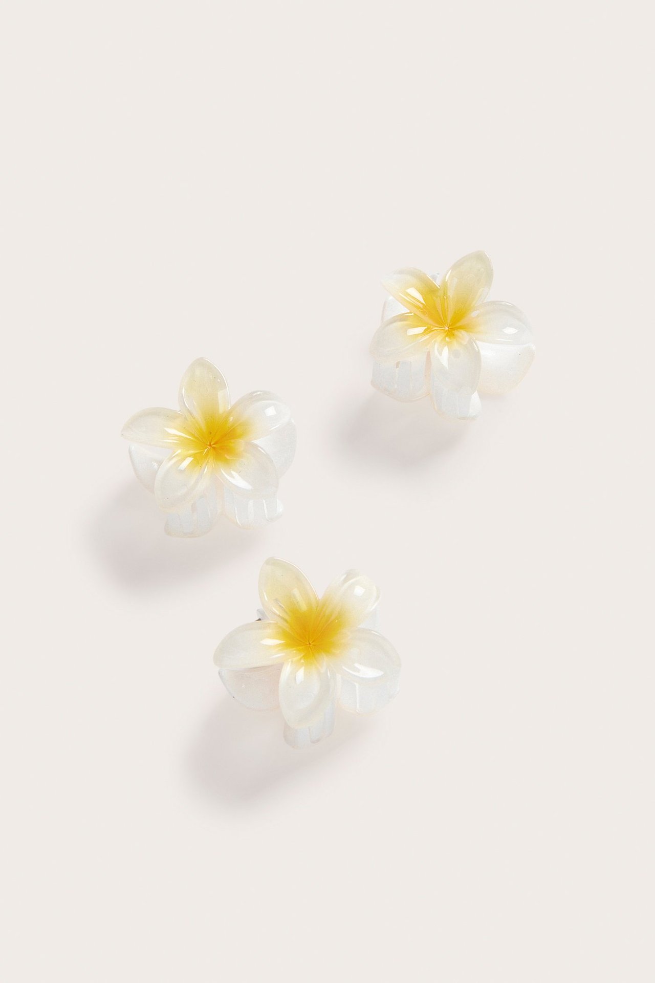 Närbild på tre genomskinliga vita blomformade hårklämmor med gula mittar, säljs i 3-pack.