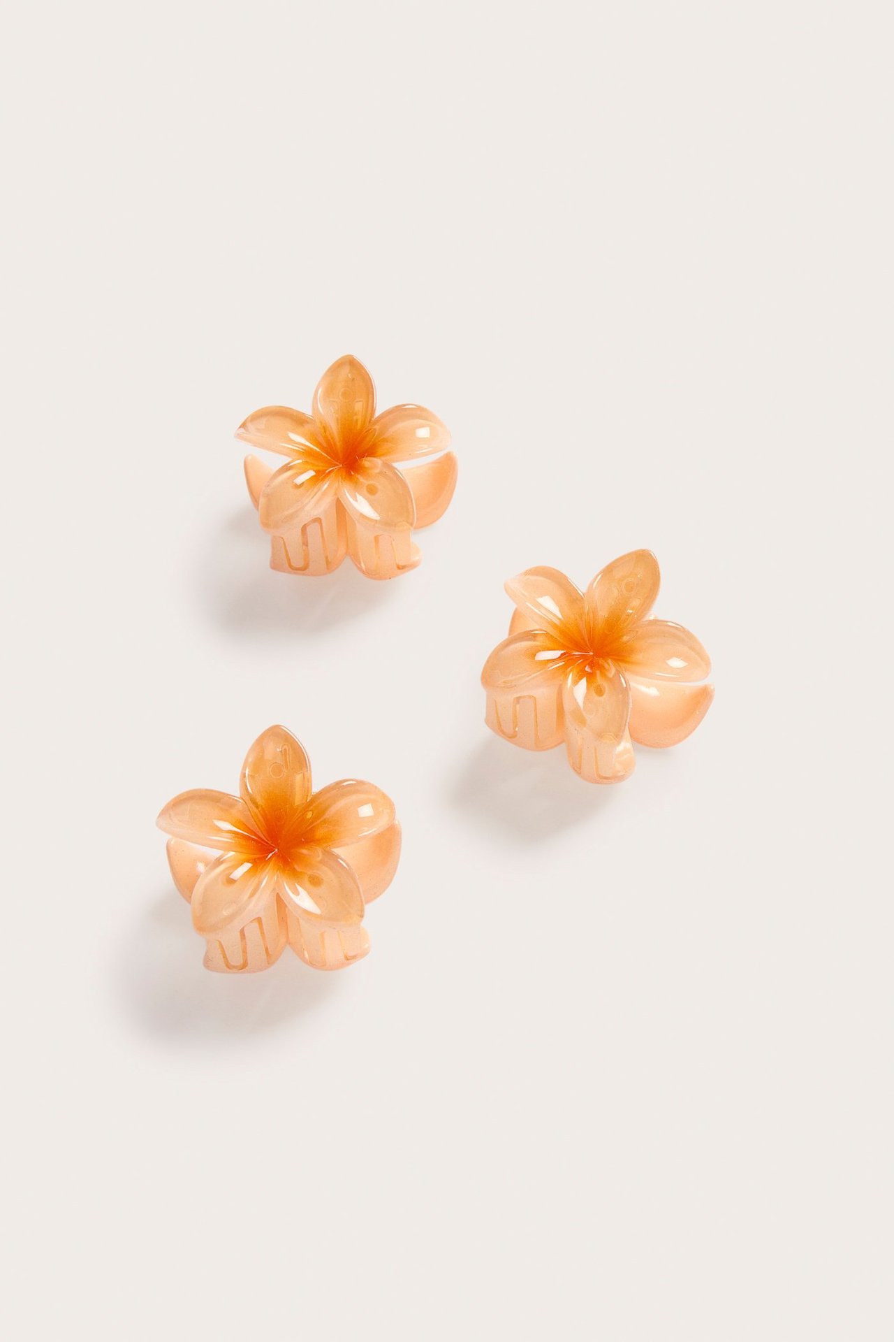 Widok z bliska trzech koralowych, kwiecistych mini spinek do włosów z przezroczystymi płatkami.