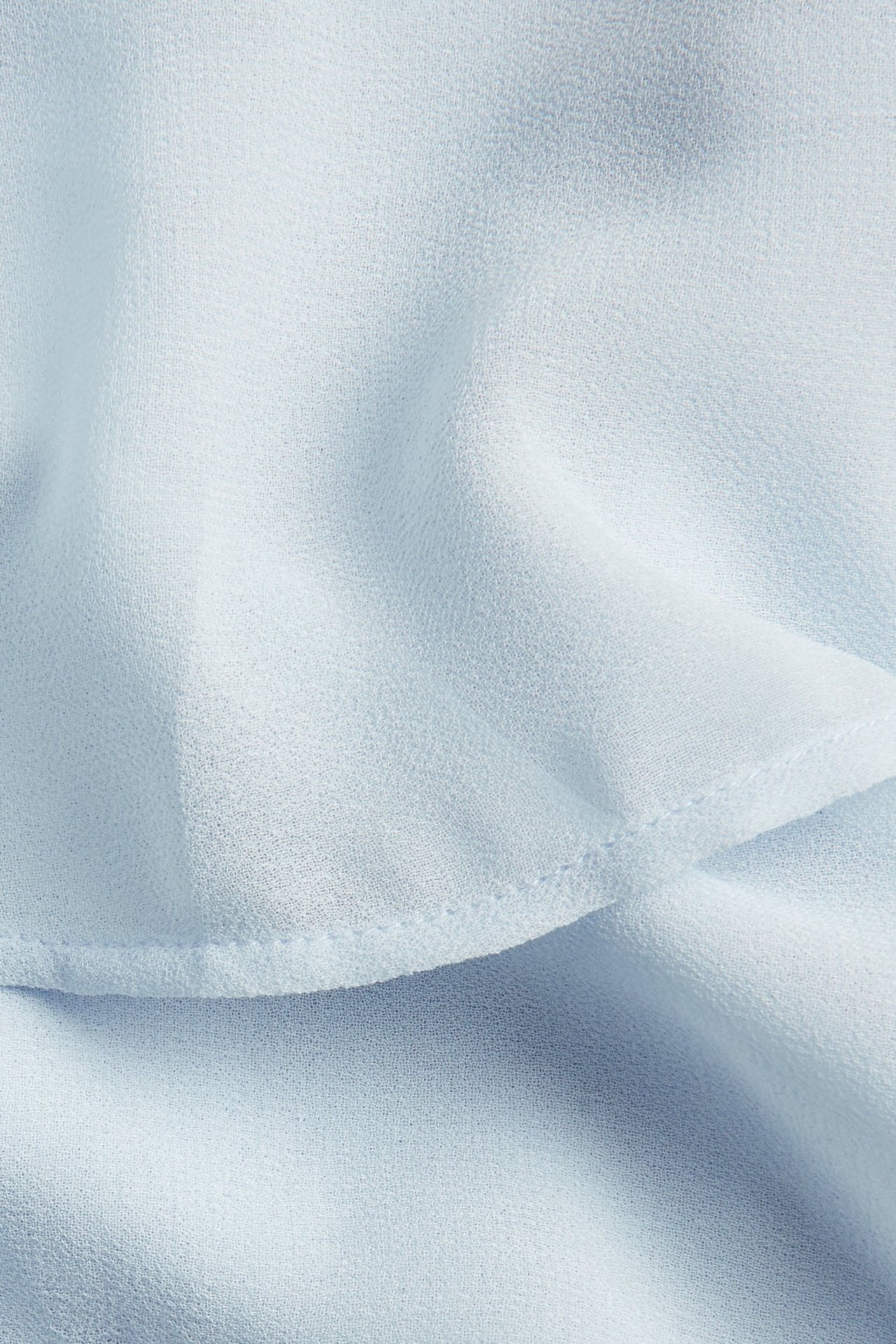 Nærbilde av lyseblått ensfarget polyesterkjolestoff med en volangkant.