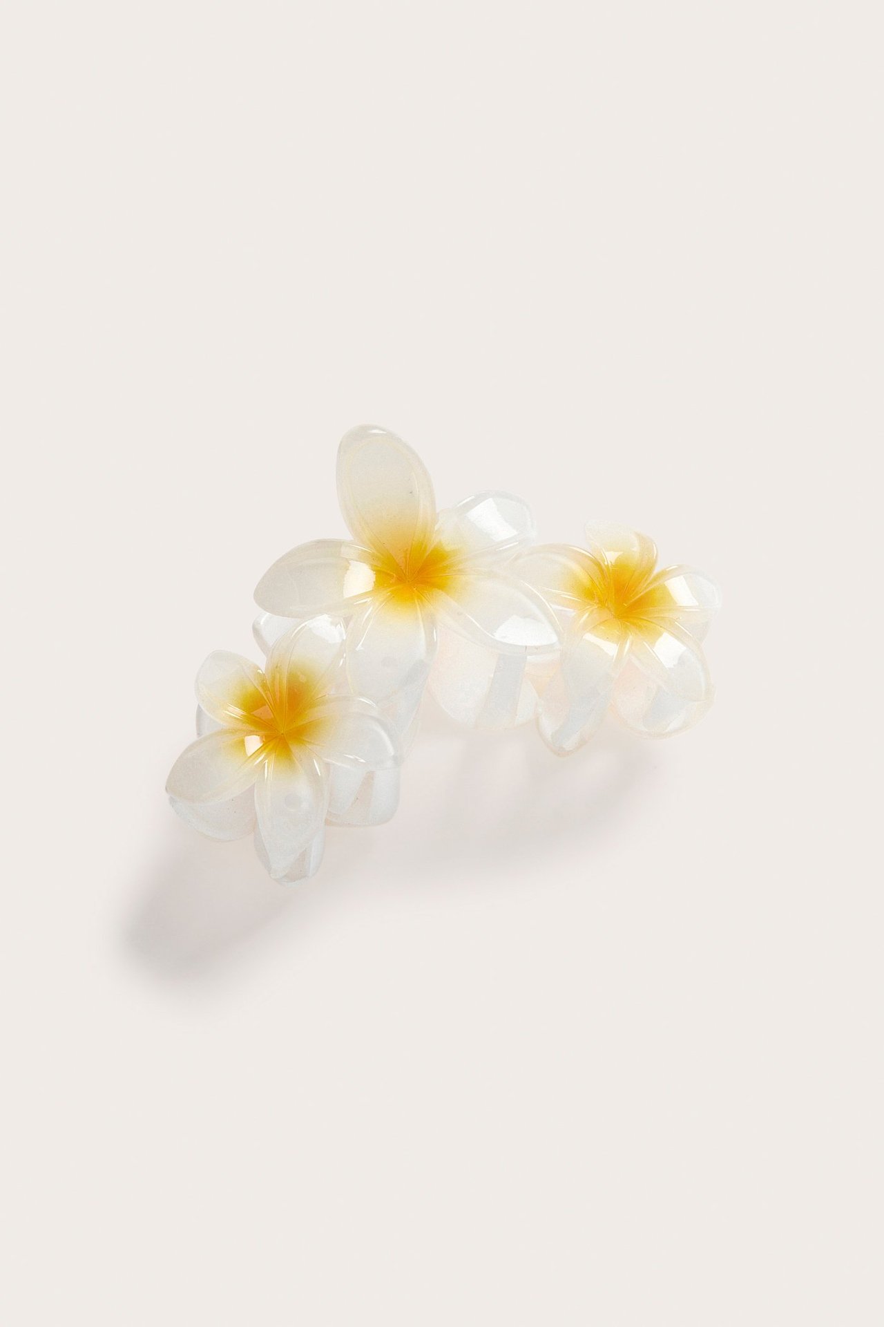 Lähikuva valkoisesta läpikuultavasta hiusklipsistä, jossa on kolme kukkaa ja keltainen keskusta.