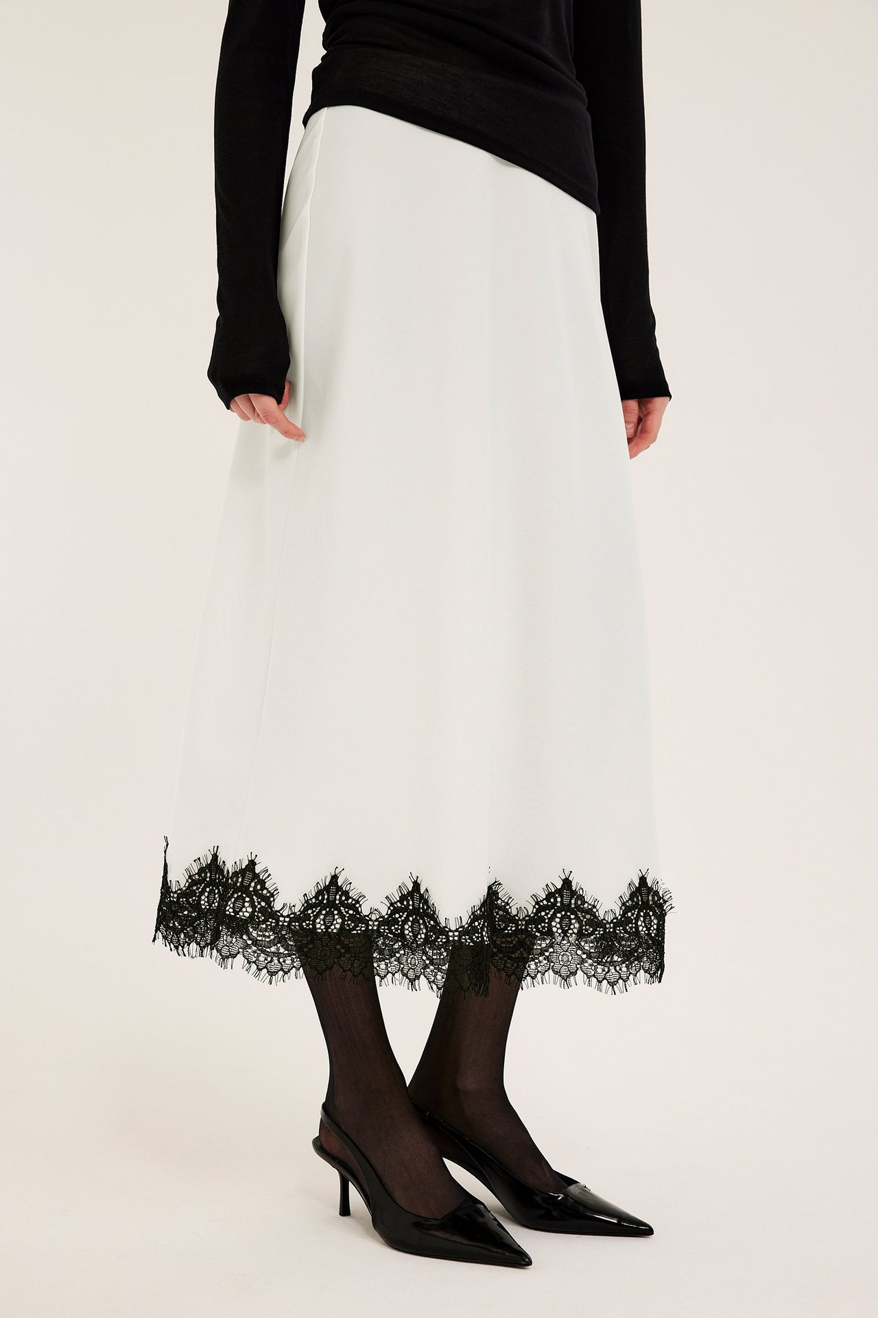Frontbilde: Offwhite satinskjørt med svarte blondedetaljer, stylet med svart topp og svarte hæler.
