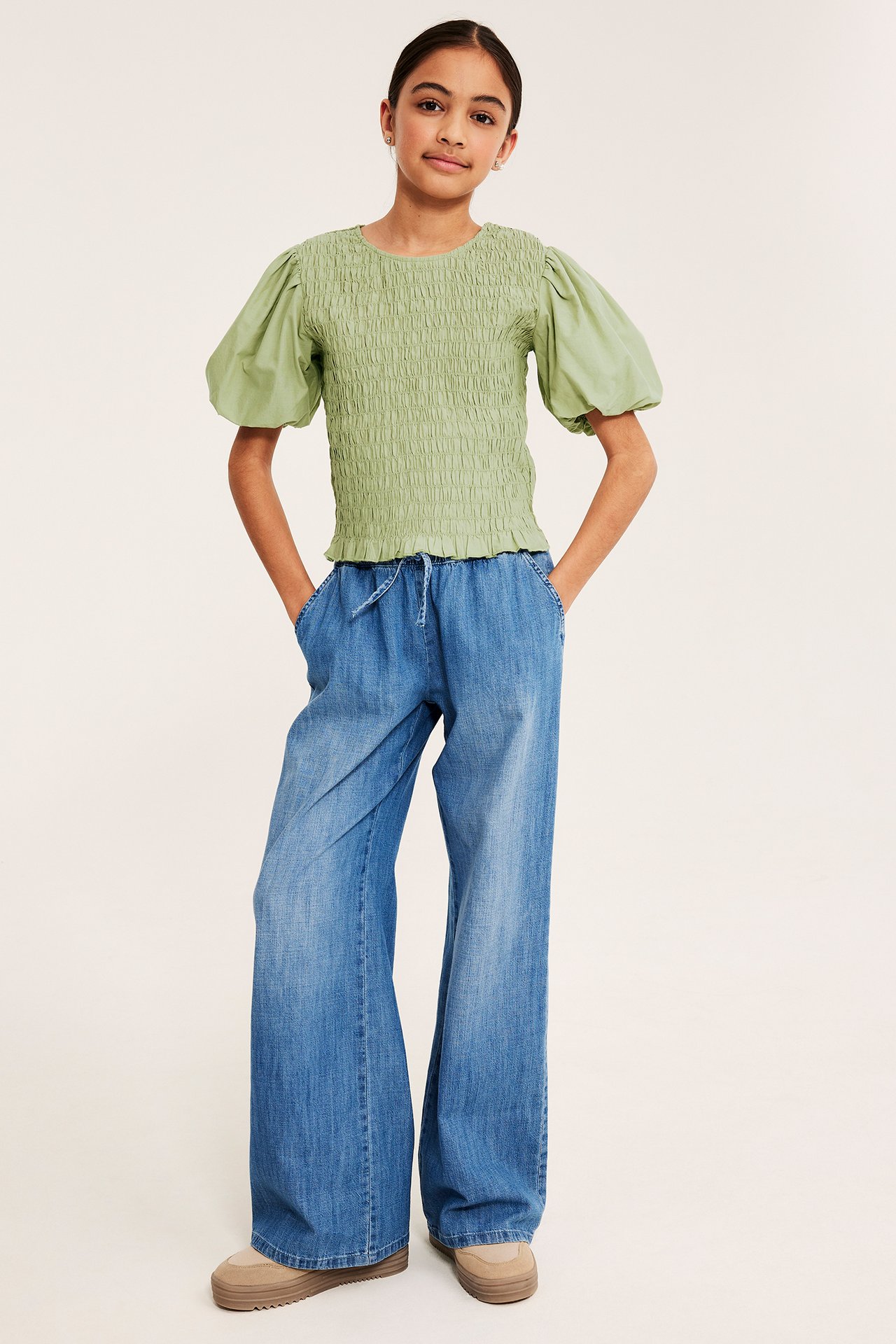 Tummanvihreä smokkitoppi puffihihoilla, siniset leveät farkut, beiget platform-kengät lapsella.