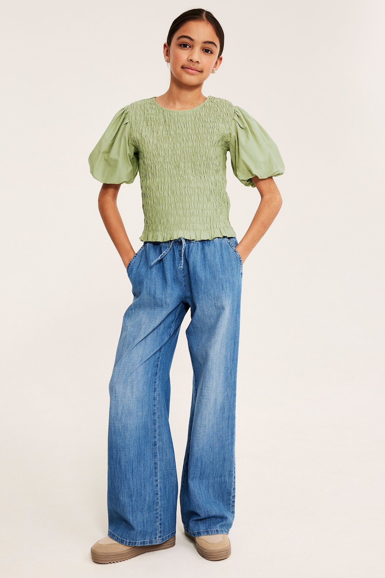 Tummanvihreä smokkitoppi puffihihoilla, siniset leveät farkut, beiget platform-kengät lapsella.