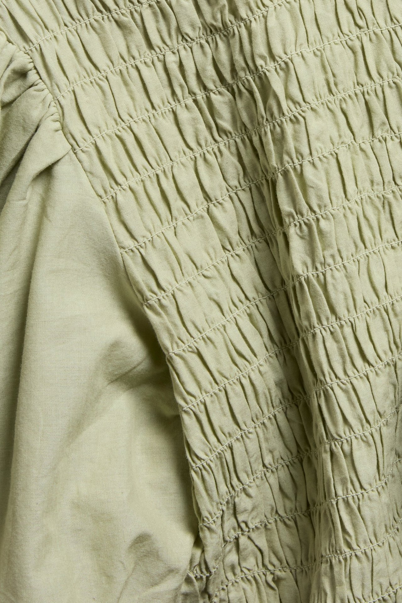 Närbild av en ljusgrön bomullstopp med smockdetaljer och en puffärm.