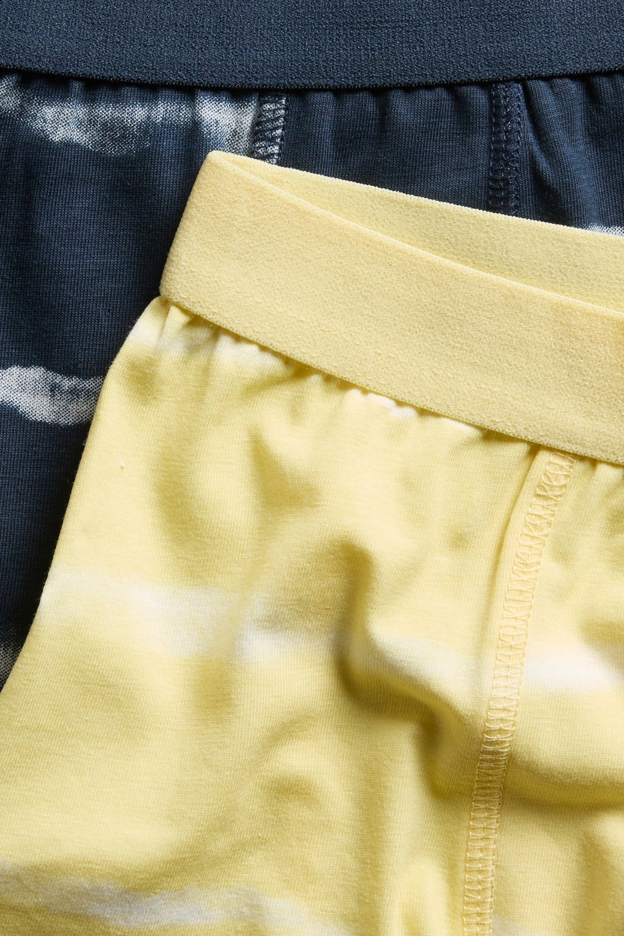 Lähikuva kelta-valkoisista batikkikuvioisista bokserishortseista keltaisella vyötärönauhalla, tummansininen batikkipari on takana.