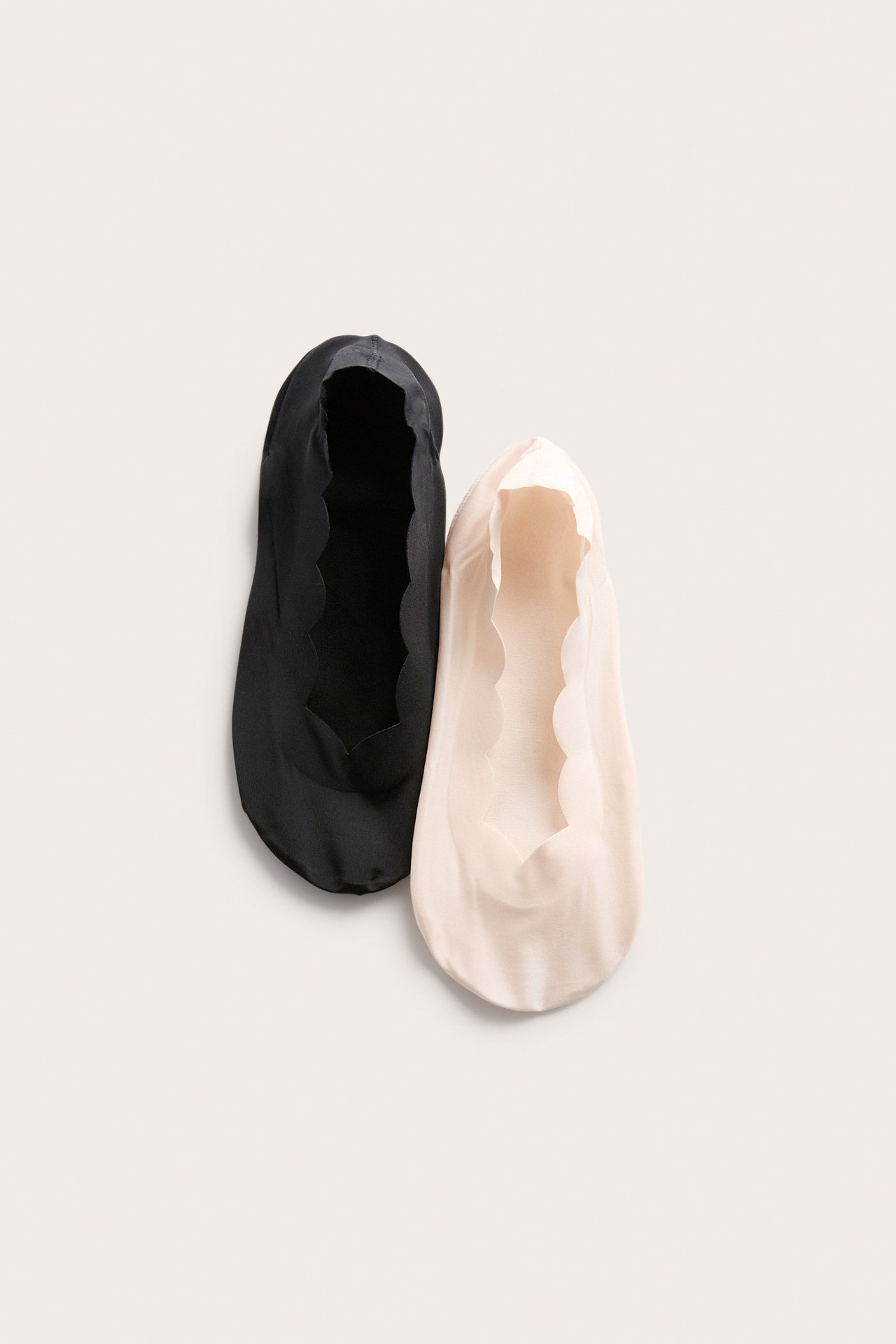 Widok z góry dwóch niewidzialnych stopek, jednej czarnej i jednej jasnobeżowej, obie z falistym brzegiem.