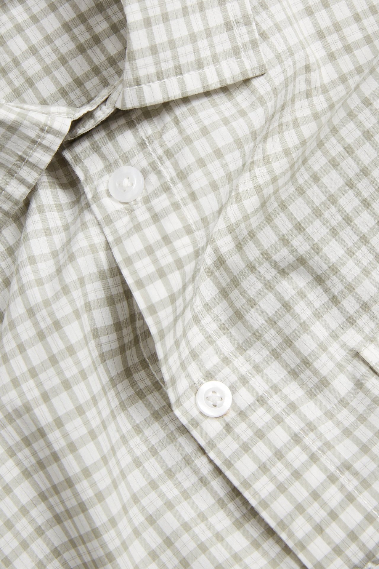 Närbild av en ljusgrön rutig kortärmad skjorta i bomullspoplin med vita knappar och bröstficka.