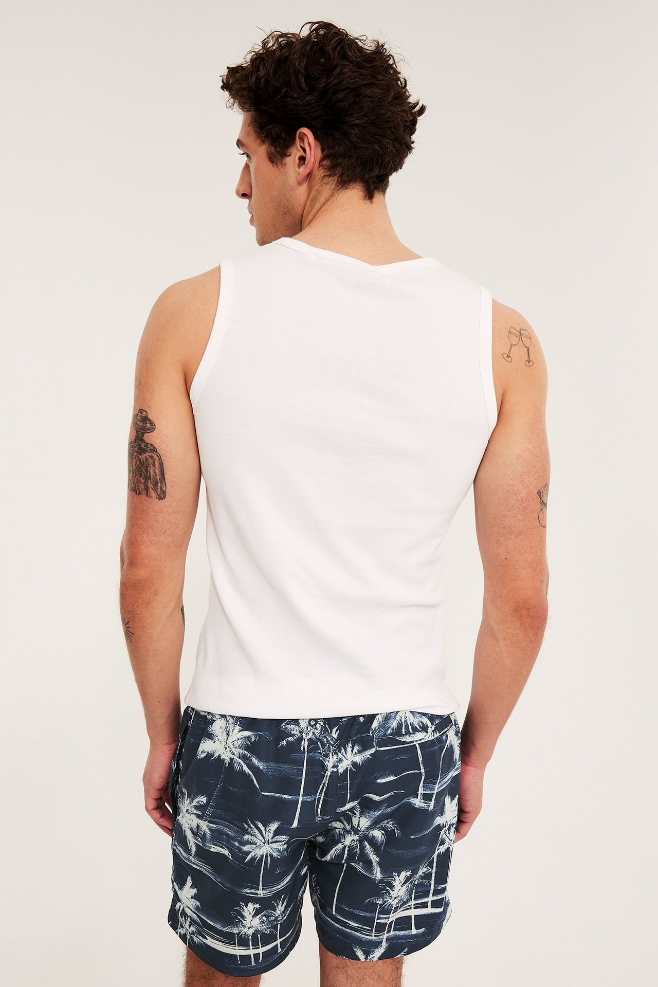 Bakifrån, man i mörkblå mönstrade badshorts med palmer och vitt linne.