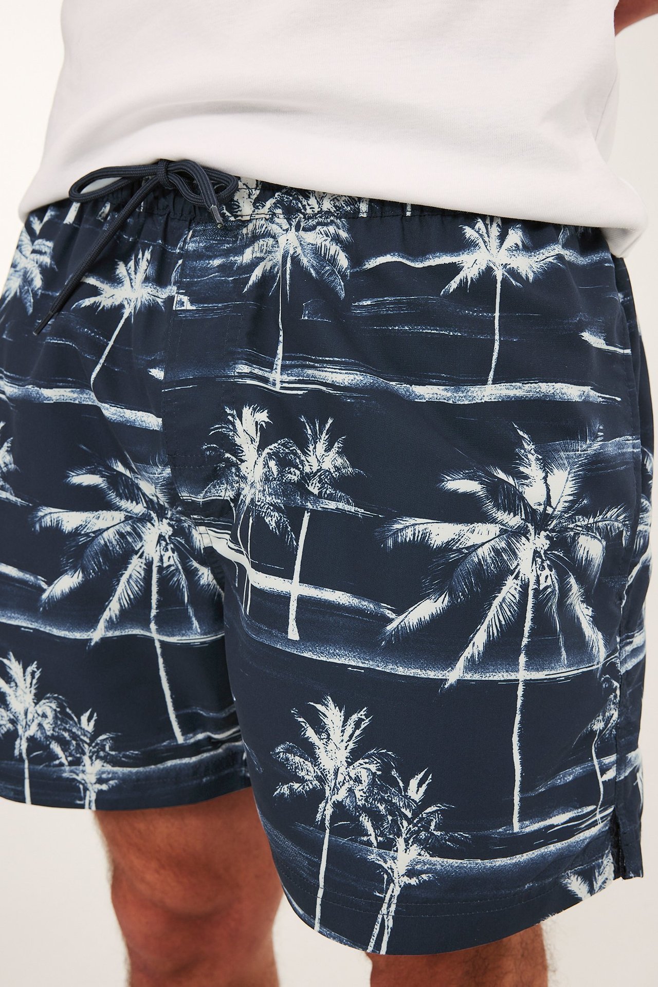 Widok z przodu granatowych szortów kąpielowych męskich z białym wzorem w palmy i sznurkiem w pasie.