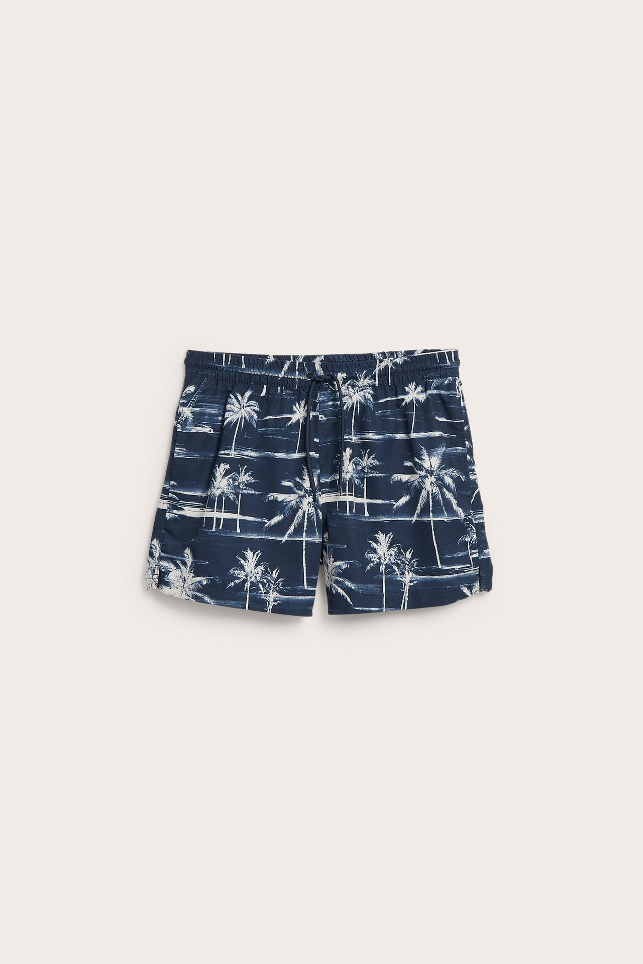 Frontvisning av mørkeblå badeshorts for menn med hvitt palmeprint, elastisk midje og snøring.