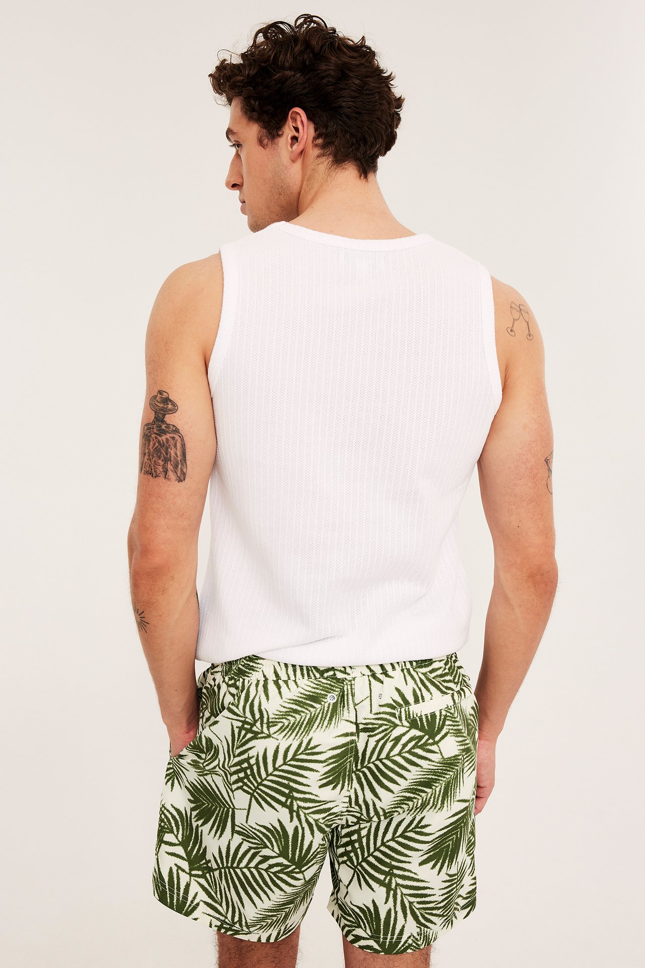 Bakifrån: Man i mönstrade khakigröna badshorts med resår och vit ribbad tank top.