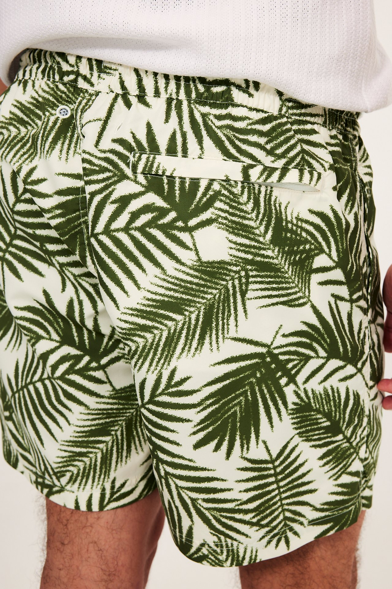 Närbild, sidovy av man i kakigröna, mönstrade badshorts med resår i midjan och bakficka med dragkedja.