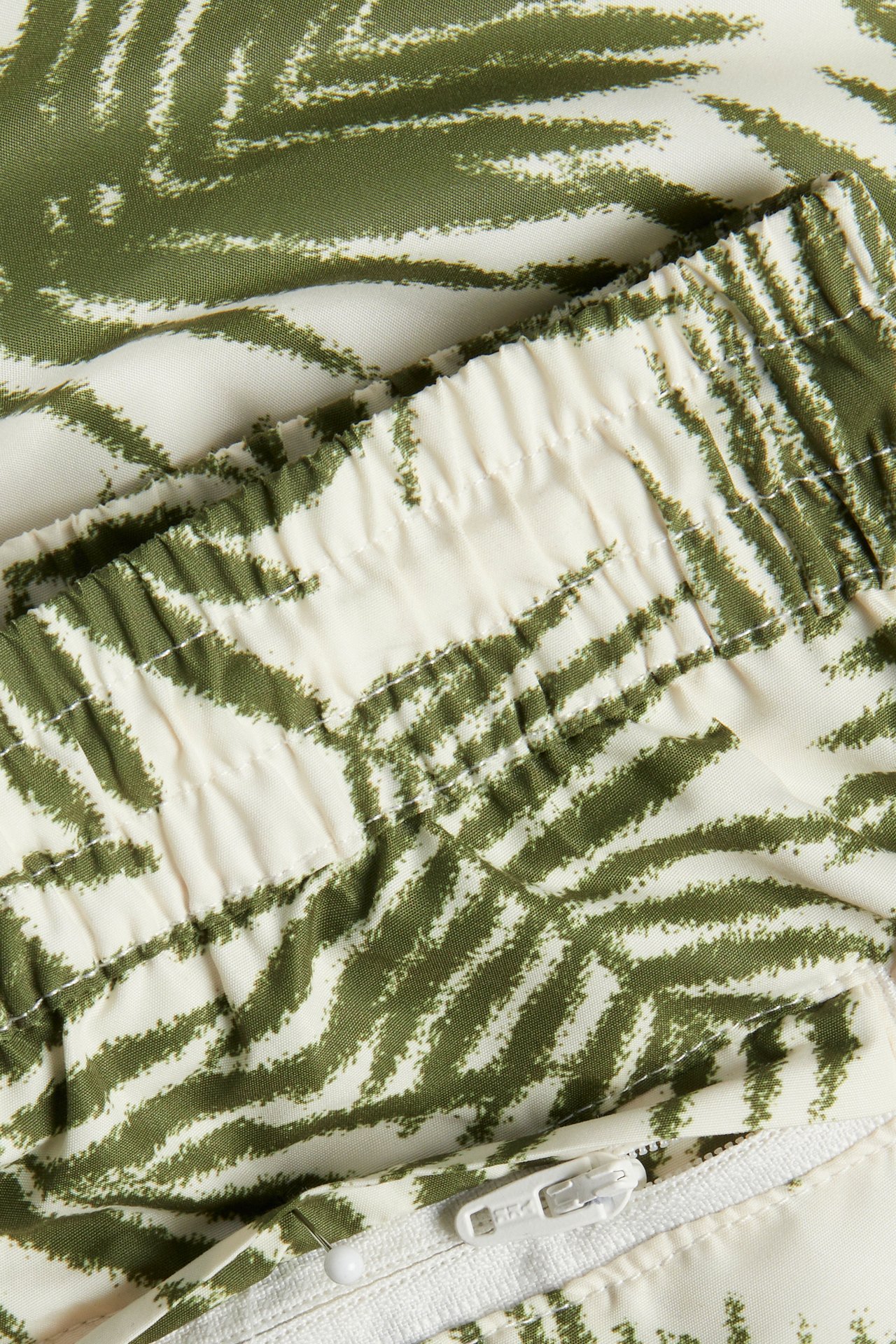 Lähikuva miesten kuvioiduista uimashortseista; khakinvihreä abstrakti kuvio, joustava vyötärö ja vetoketju.