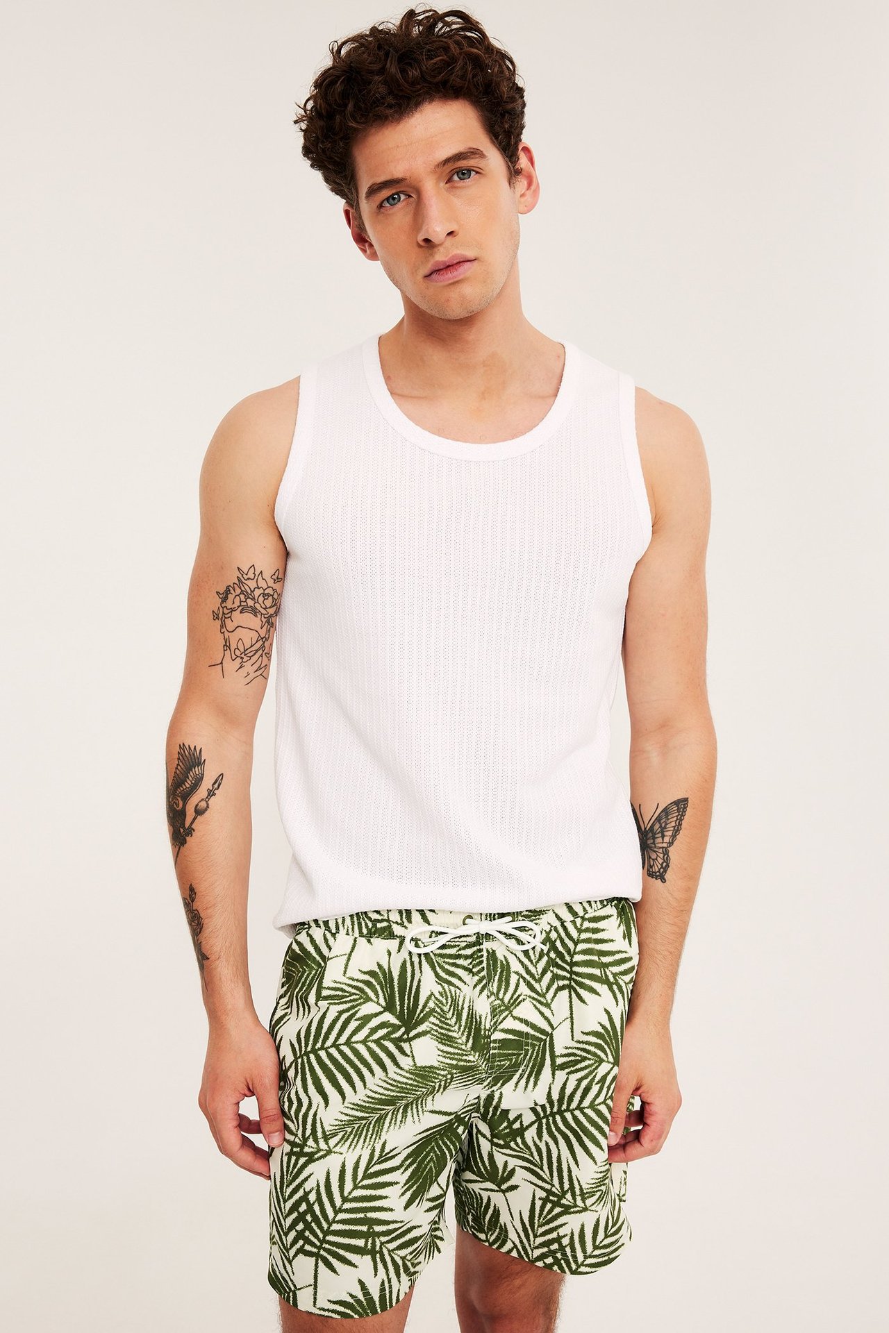 Forfra: Mann i grønne palmbladsmønstrede badeshorts med snøring i midjen og en hvit singlet.