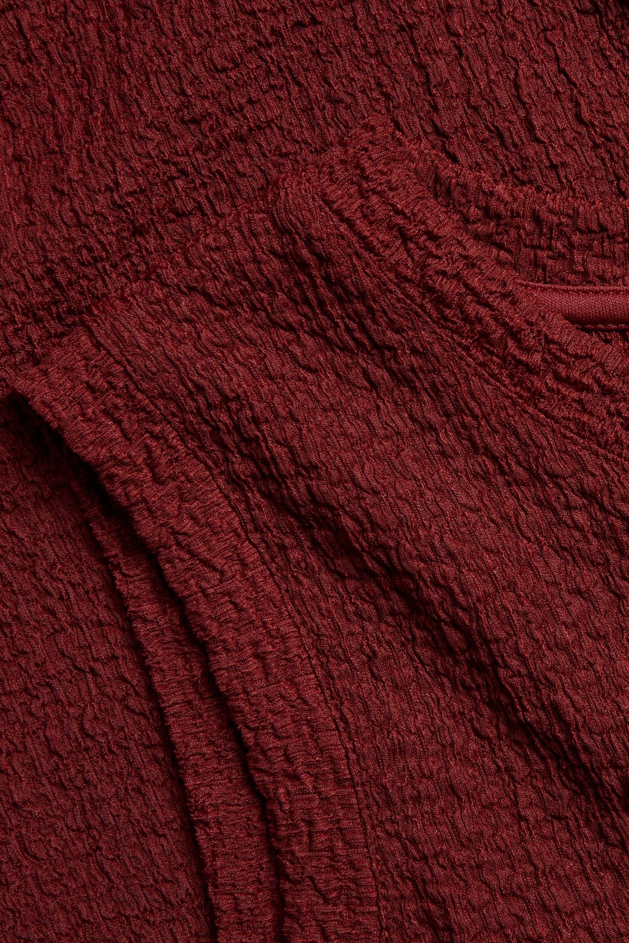 Närbild på det röda strukturerade tyget från en ärmlös midiklänning.