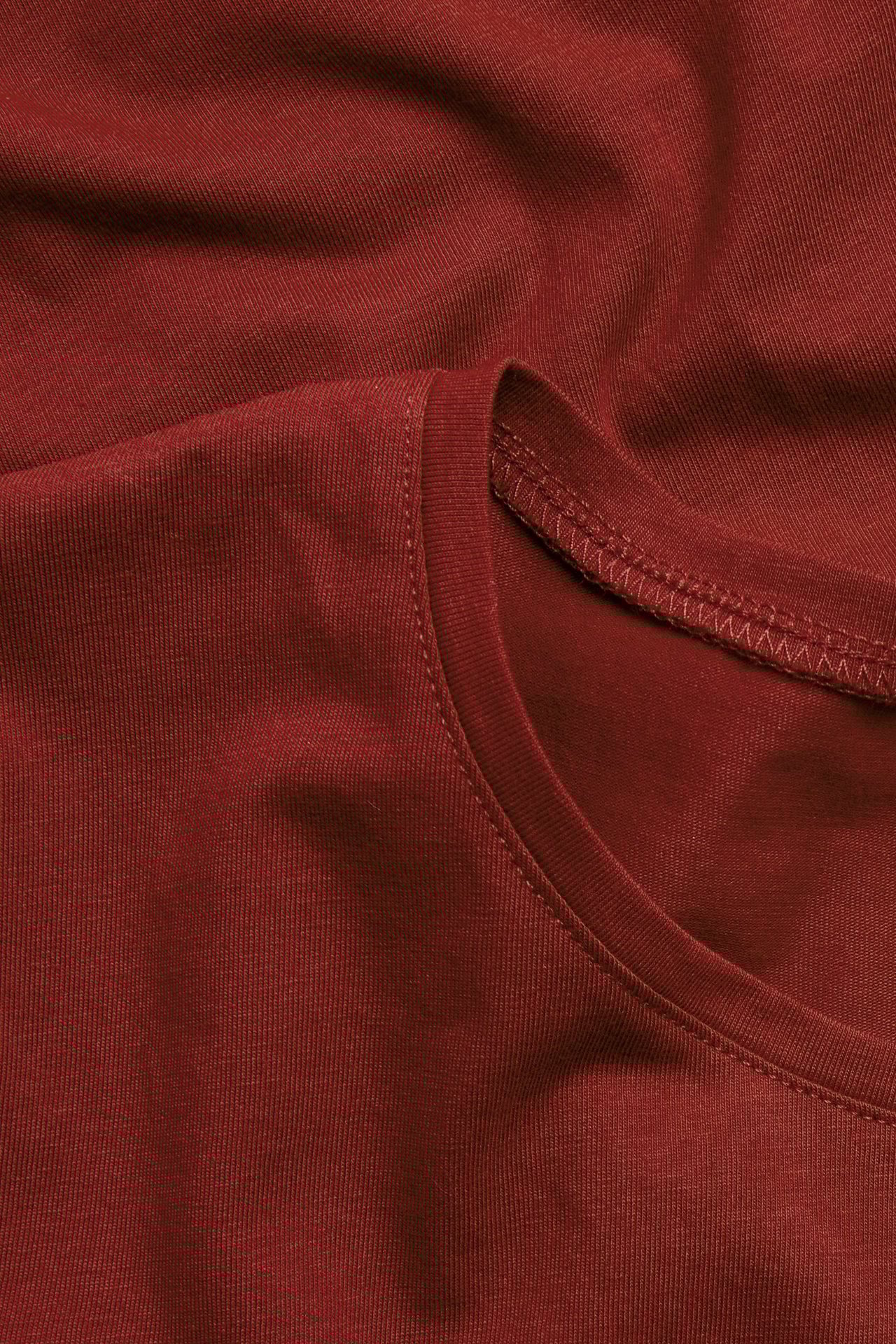 Zbliżenie złożonego, jednolicie czerwonego, podstawowego topu z krótkim rękawem i okrągłym dekoltem.