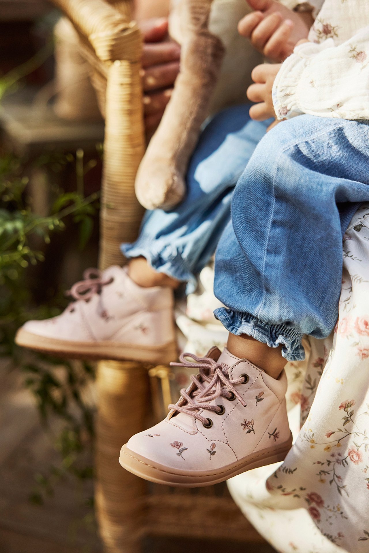 Nærbilde: baby bruker lys rosa blomstrete skinnsko, blå rysjete denim bukser.