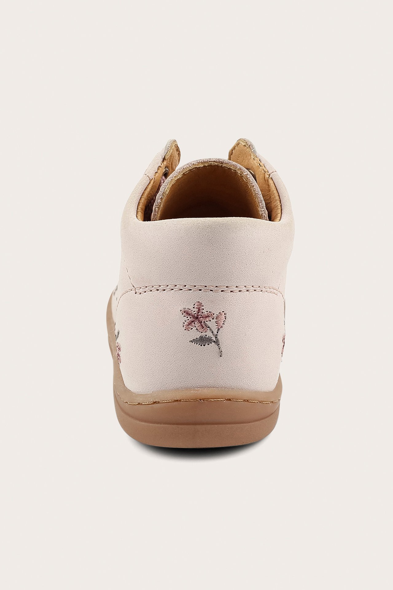 Vaaleanpunainen lasten kävelykenkä takaa, pienellä vaaleanpunaisella kukkakirjonnalla ja ruskealla pohjalla.