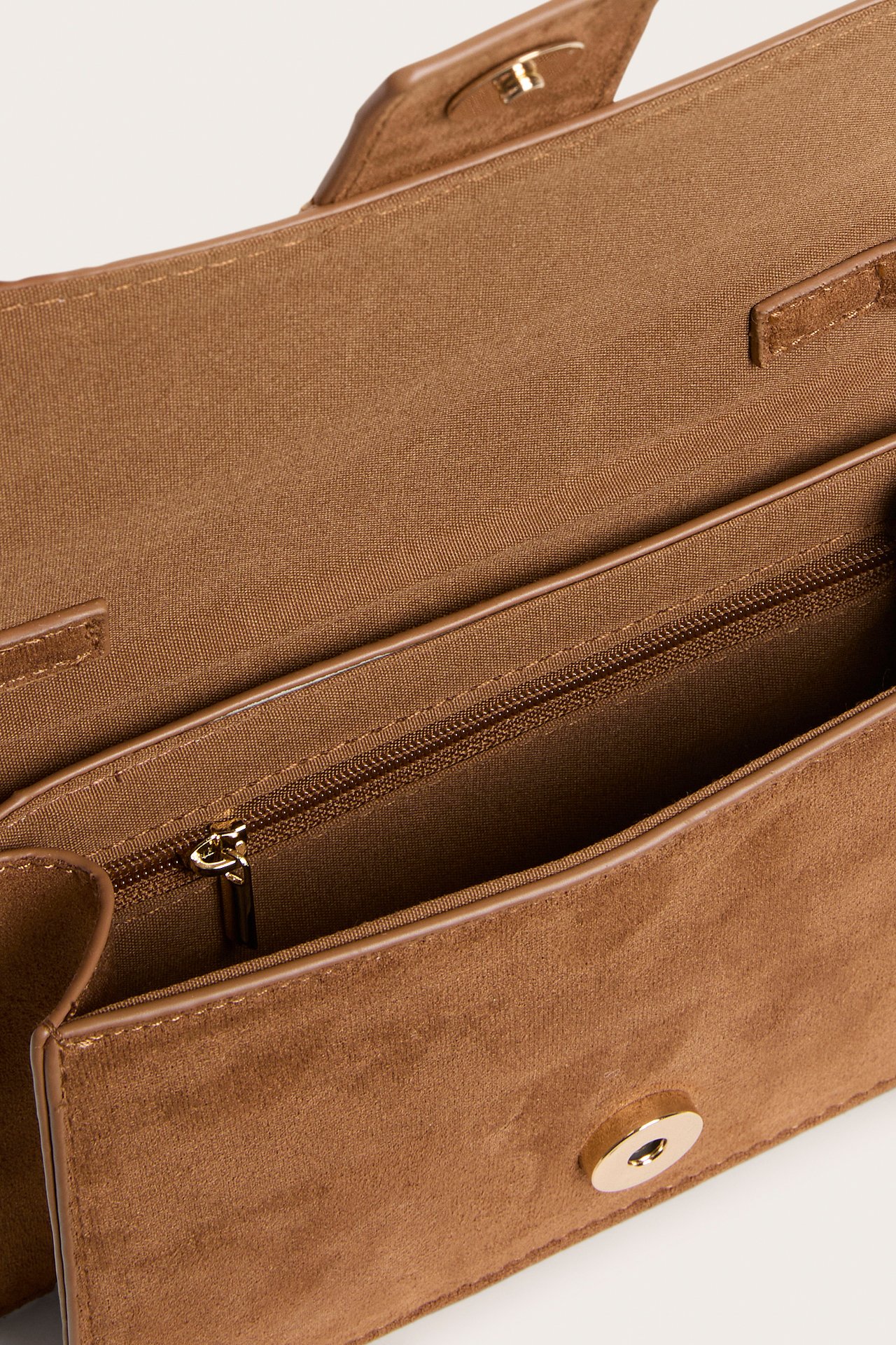 Nærbilde, ovenfra: brun imitert semsket skinn skulderveske, delvis åpen, viser magnetlås og glidelås.