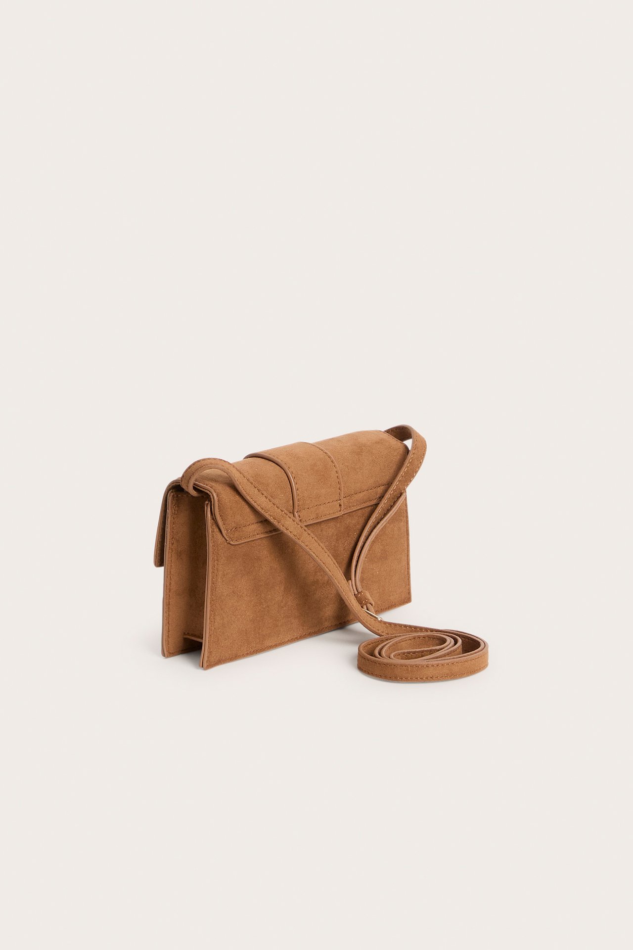 Sidebilde av en liten brun skulderveske i semsket imitasjon med klaff.