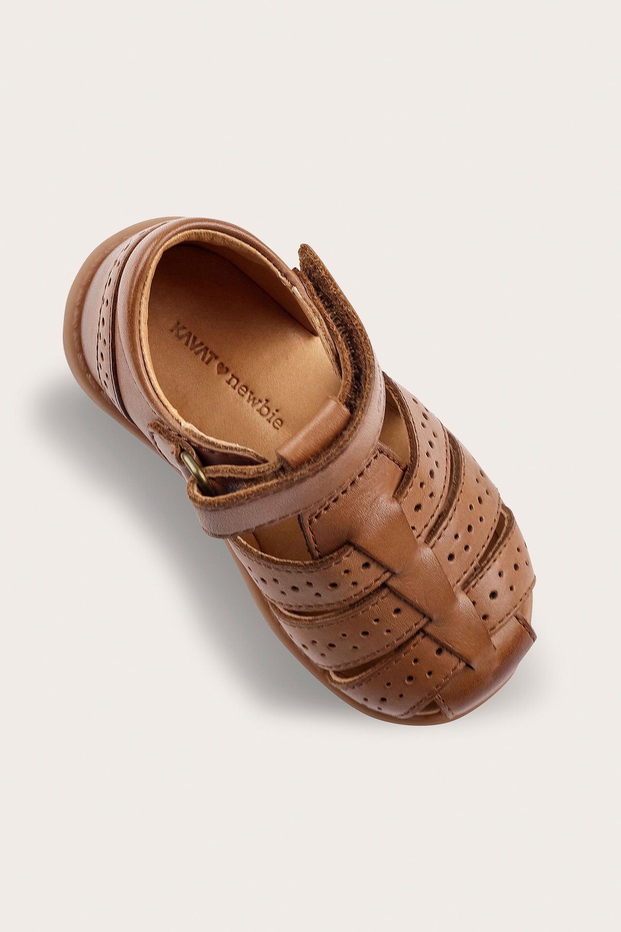 Hög vinkelvy av en brun läder barnsandal med stängd tå, perforerade detaljer och kardborreband.