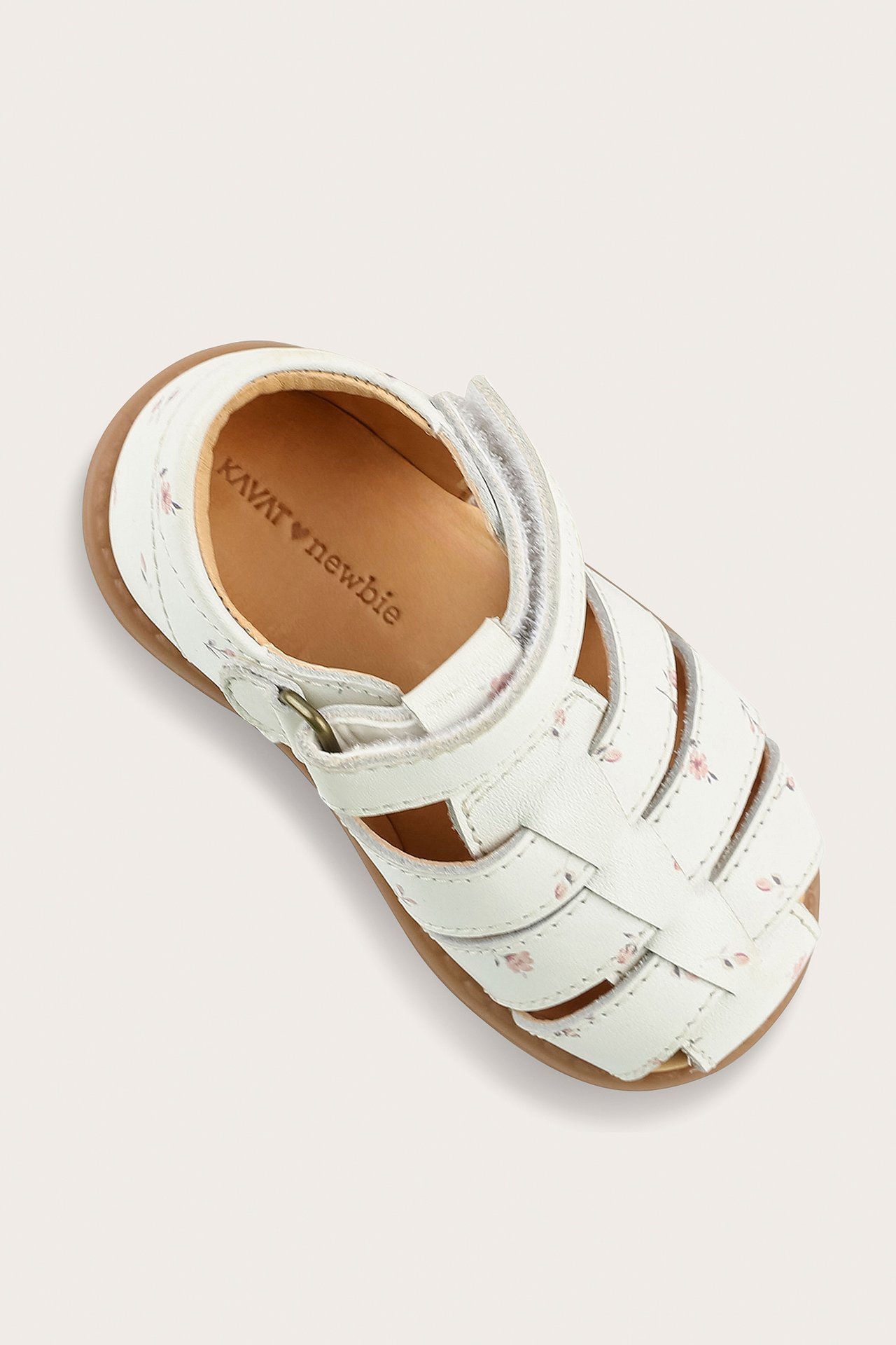 Närbild på en vit baby-sandal i läder med rosa blommönster och kardborreknäppning.