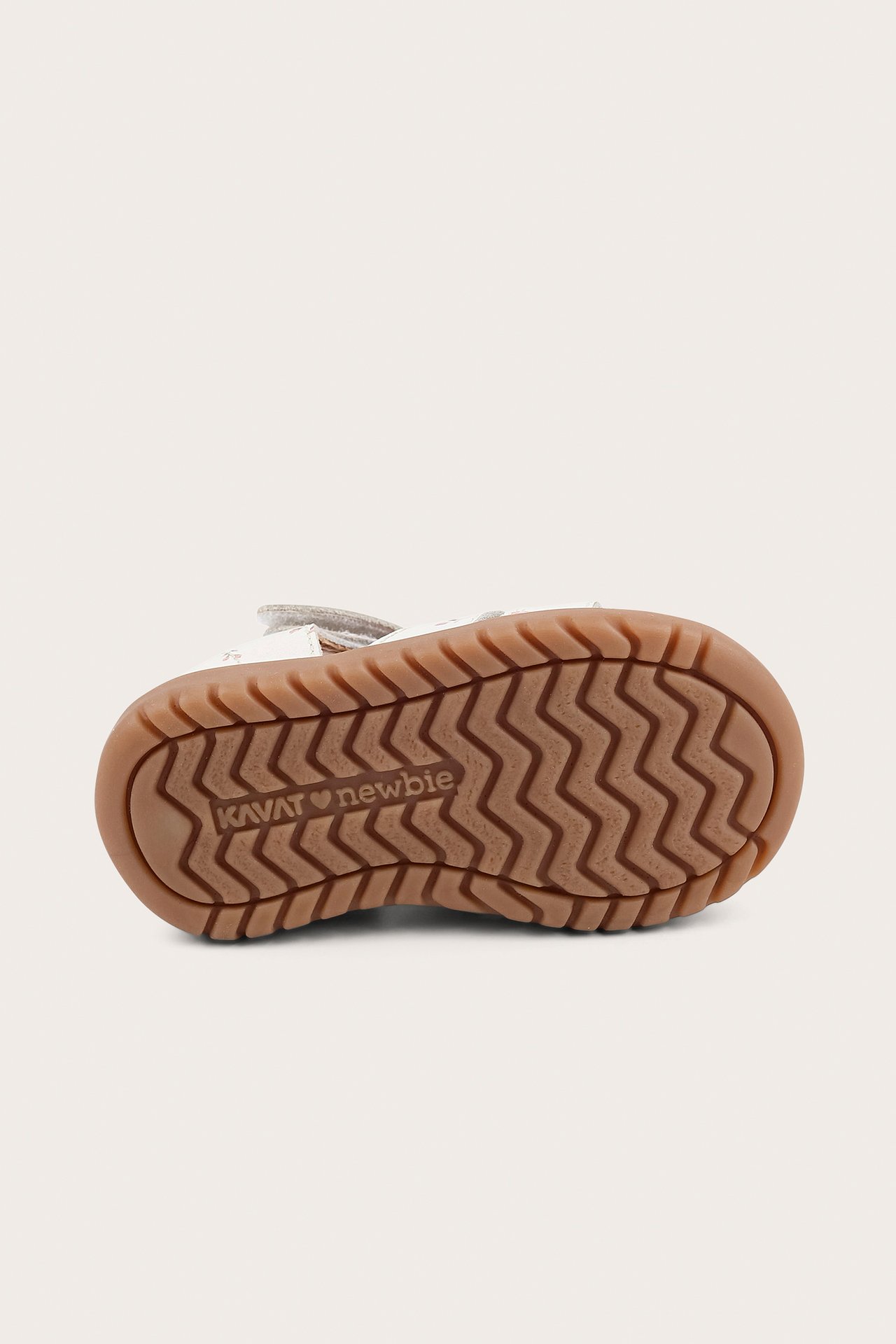 Bottenvy av en vit blommig kidsandal med en framträdande vågig brun gummisula.