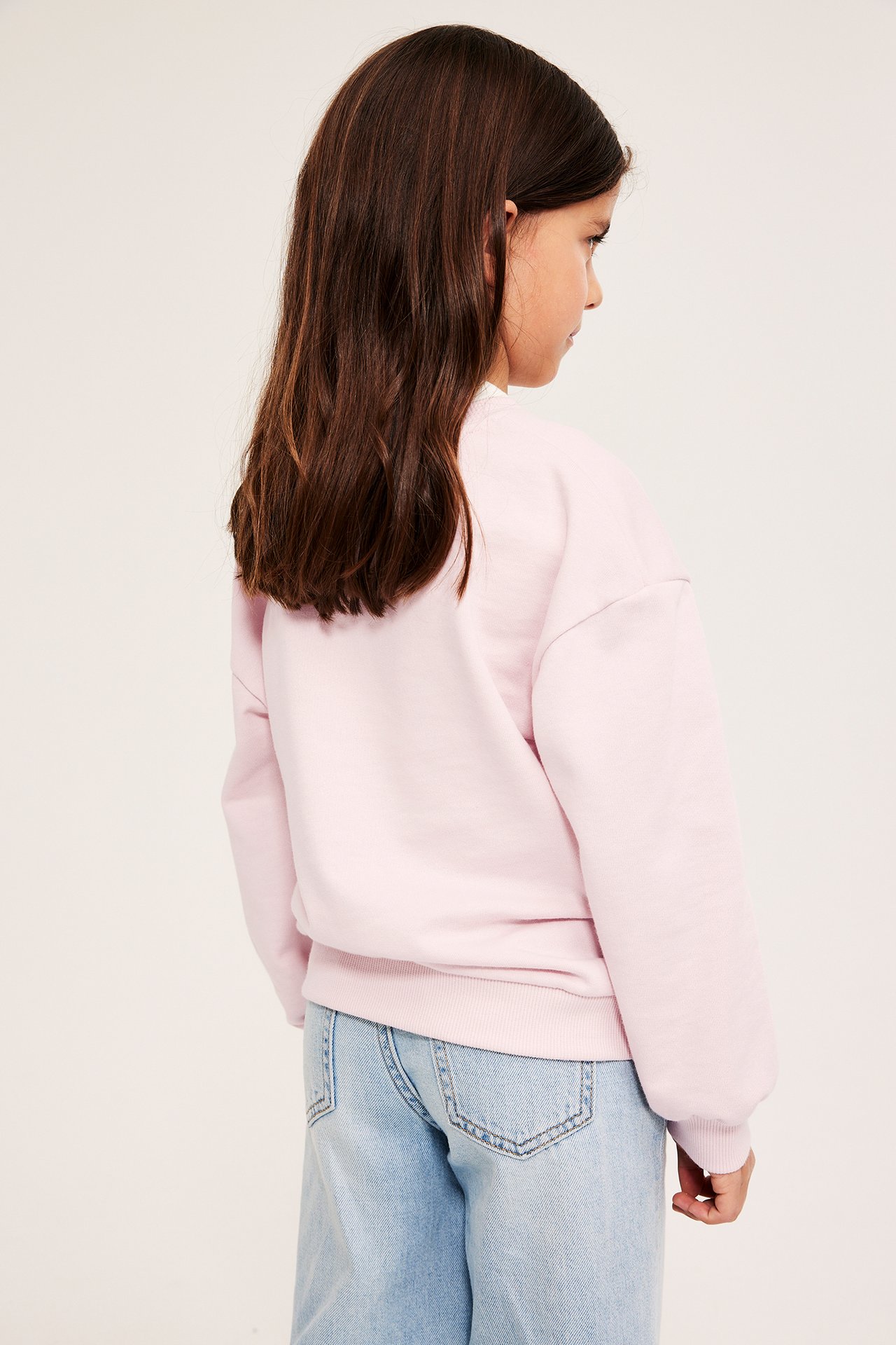 Sivukuva lapsesta yllään vaaleanpunainen puuvillasekoitepusero ja vaaleansiniset farkut.